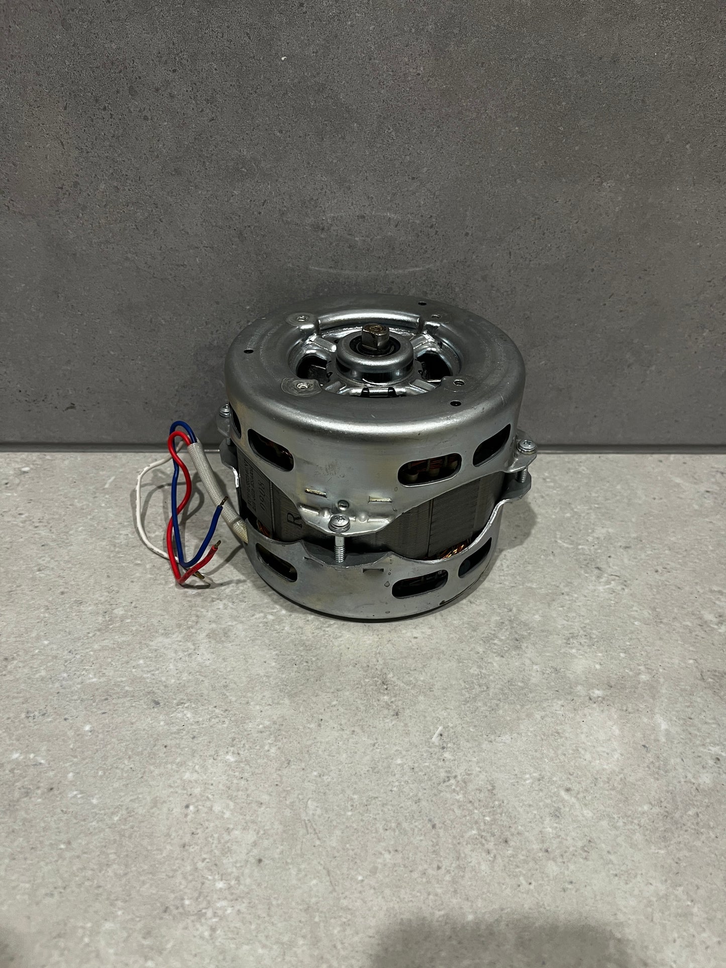 Compact electric motor with metal casing and color-coded wiring on a stone surface
