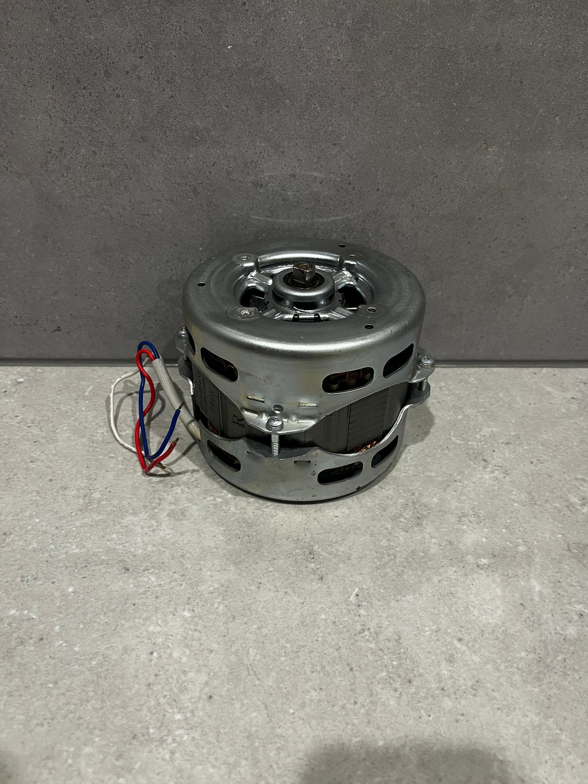 Compact electric motor with metal casing and color-coded wiring on a stone surface