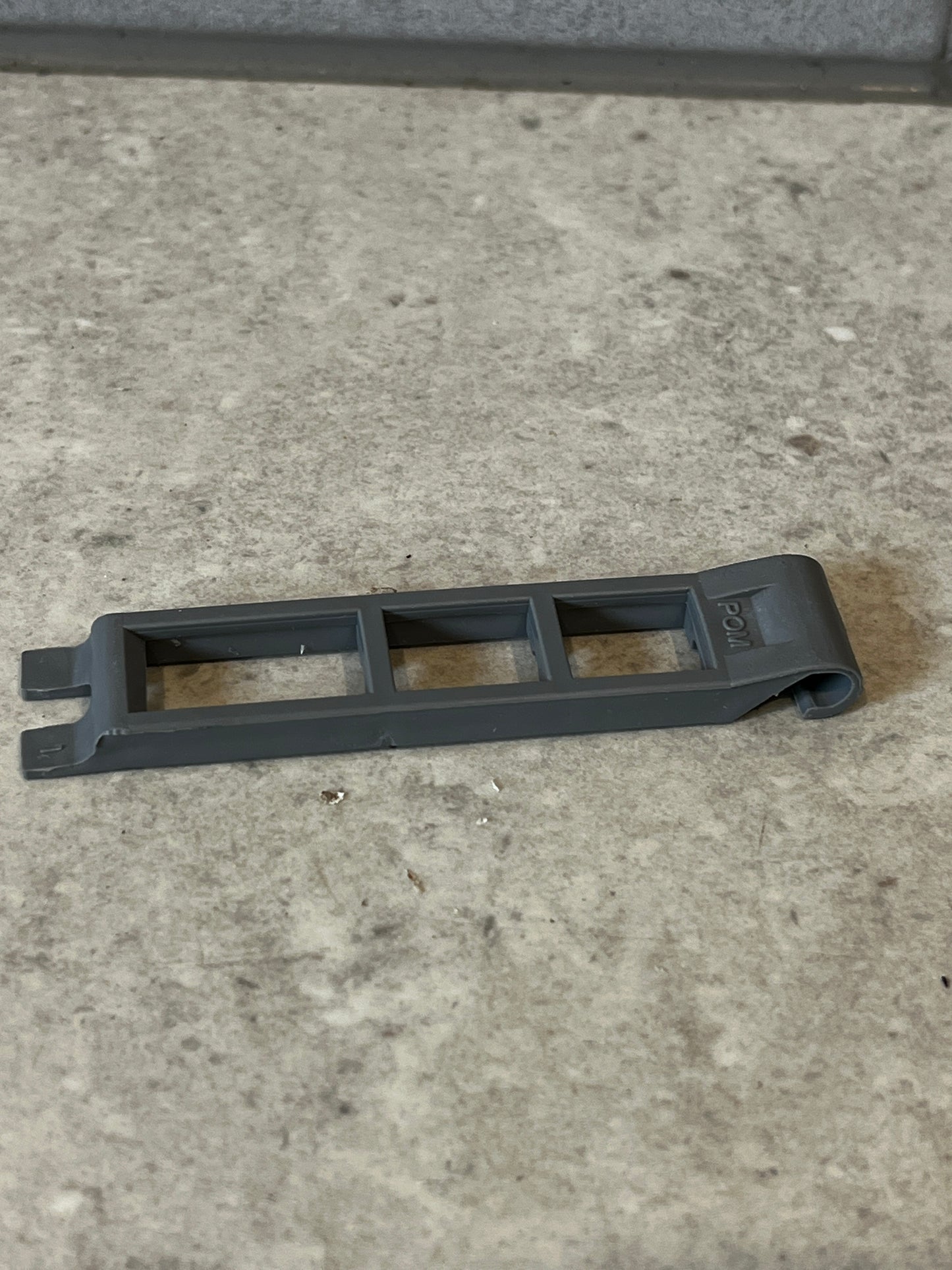 Gray plastic spacer tool with open-frame design lying on a stone surface