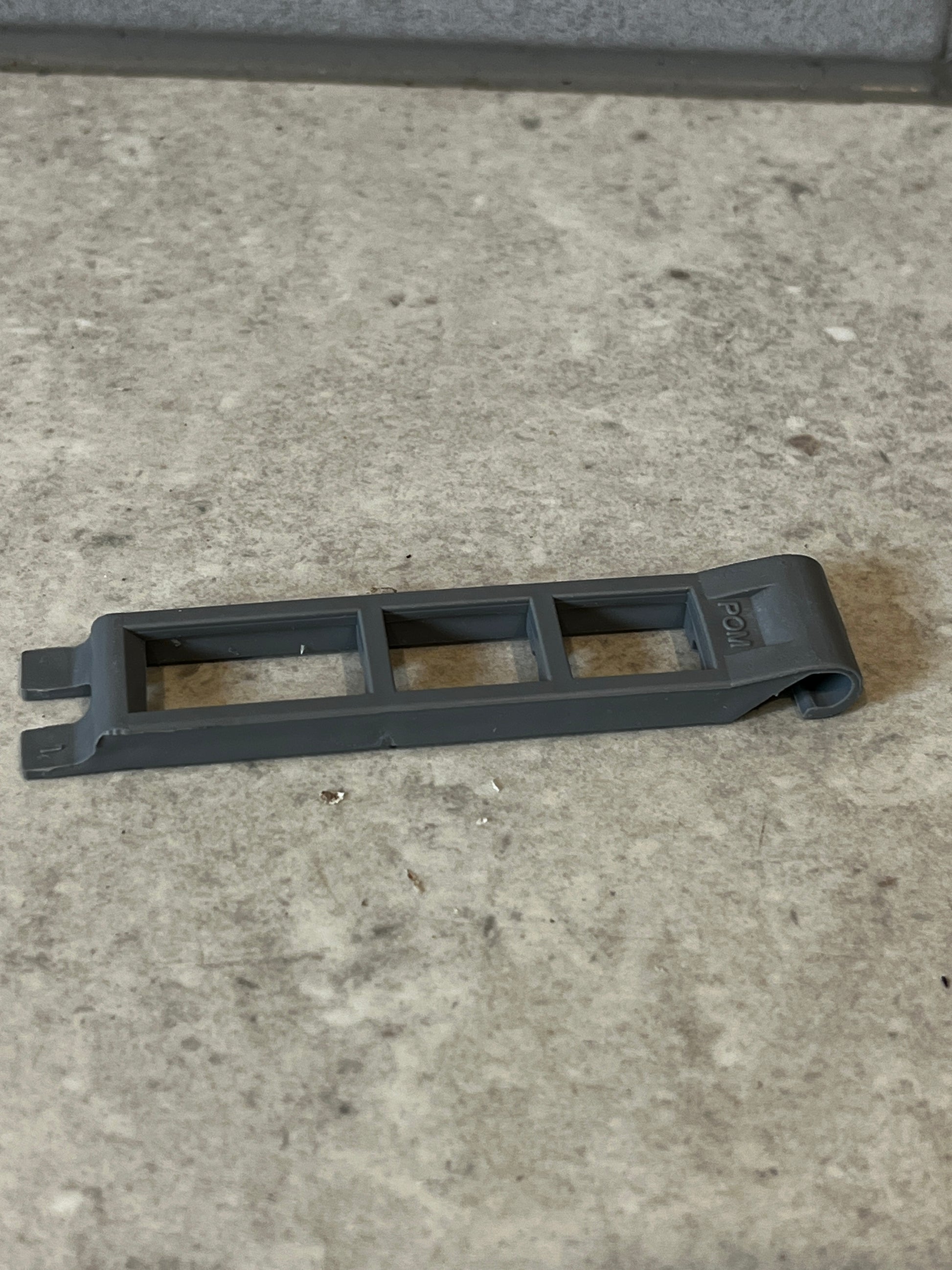 Gray plastic spacer tool with open-frame design lying on a stone surface