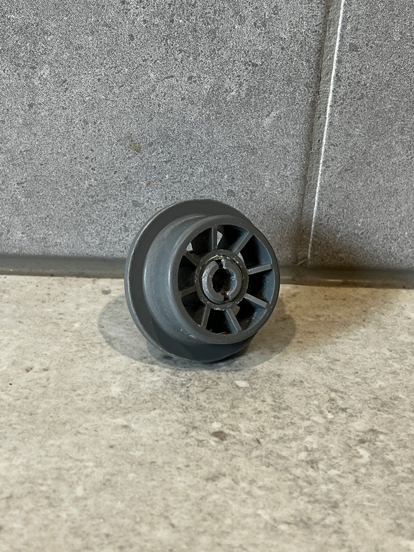 Gray plastic dishwasher lower rack wheel viewed from the side showing the wheel and central hole