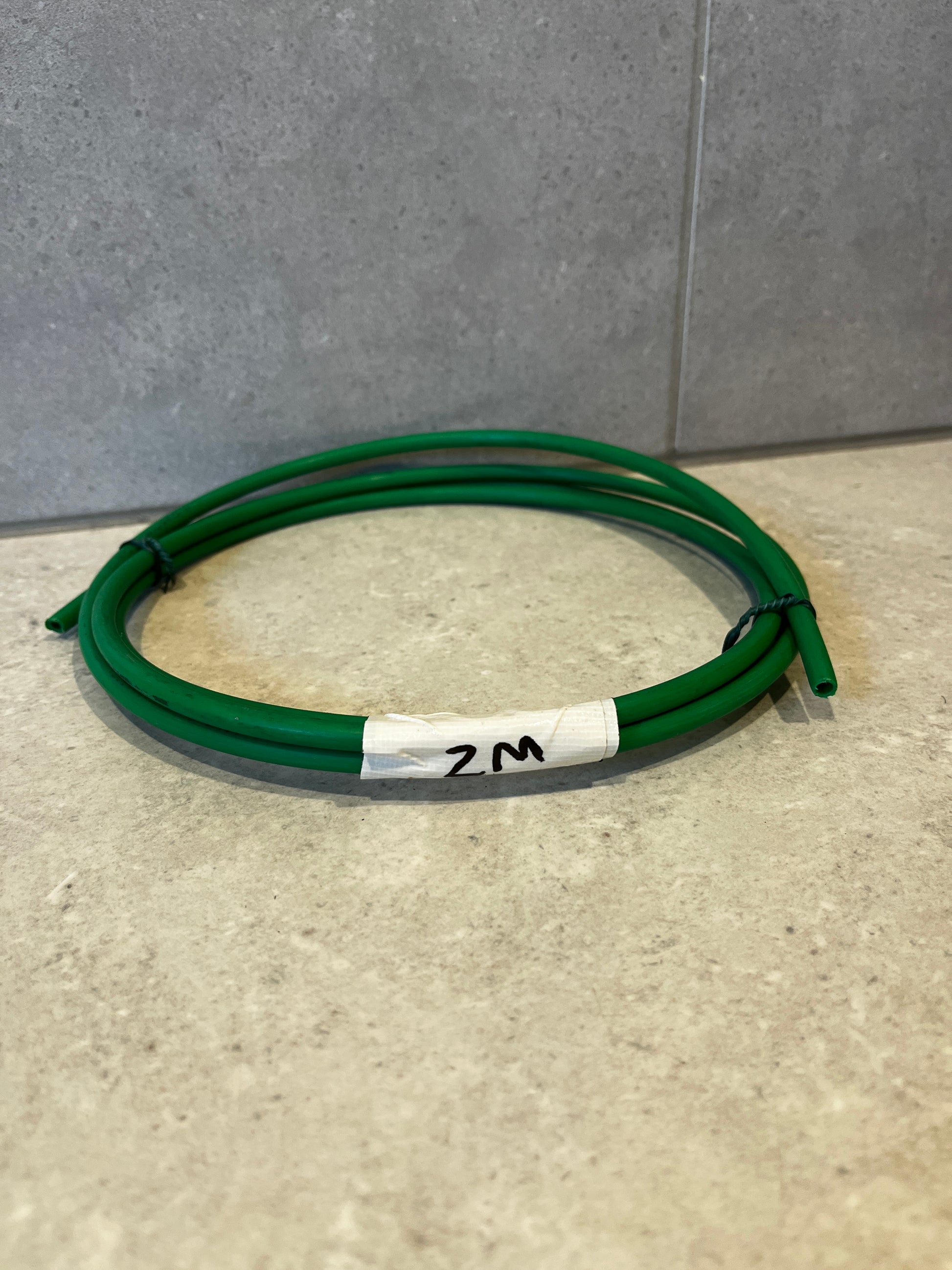 Green plastic tubing hose coiled on a countertop with length label '2M'