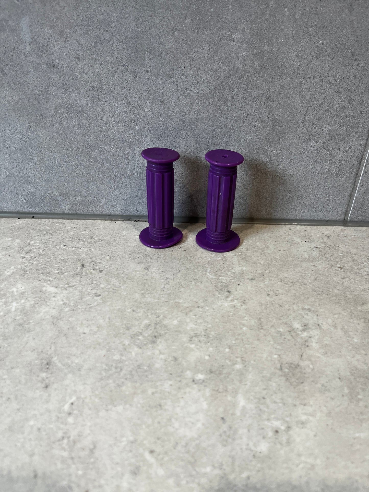 Pair of purple rubber handlebar grips on a gray tiled surface.