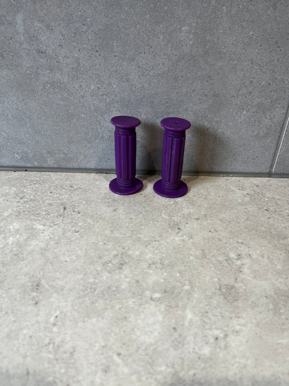 Pair of purple rubber handlebar grips on a gray tiled surface.