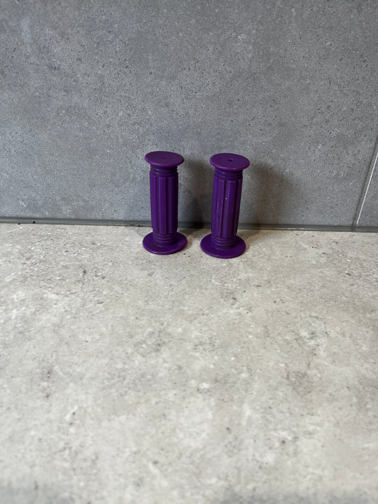 Pair of purple rubber handlebar grips on a gray tiled surface.