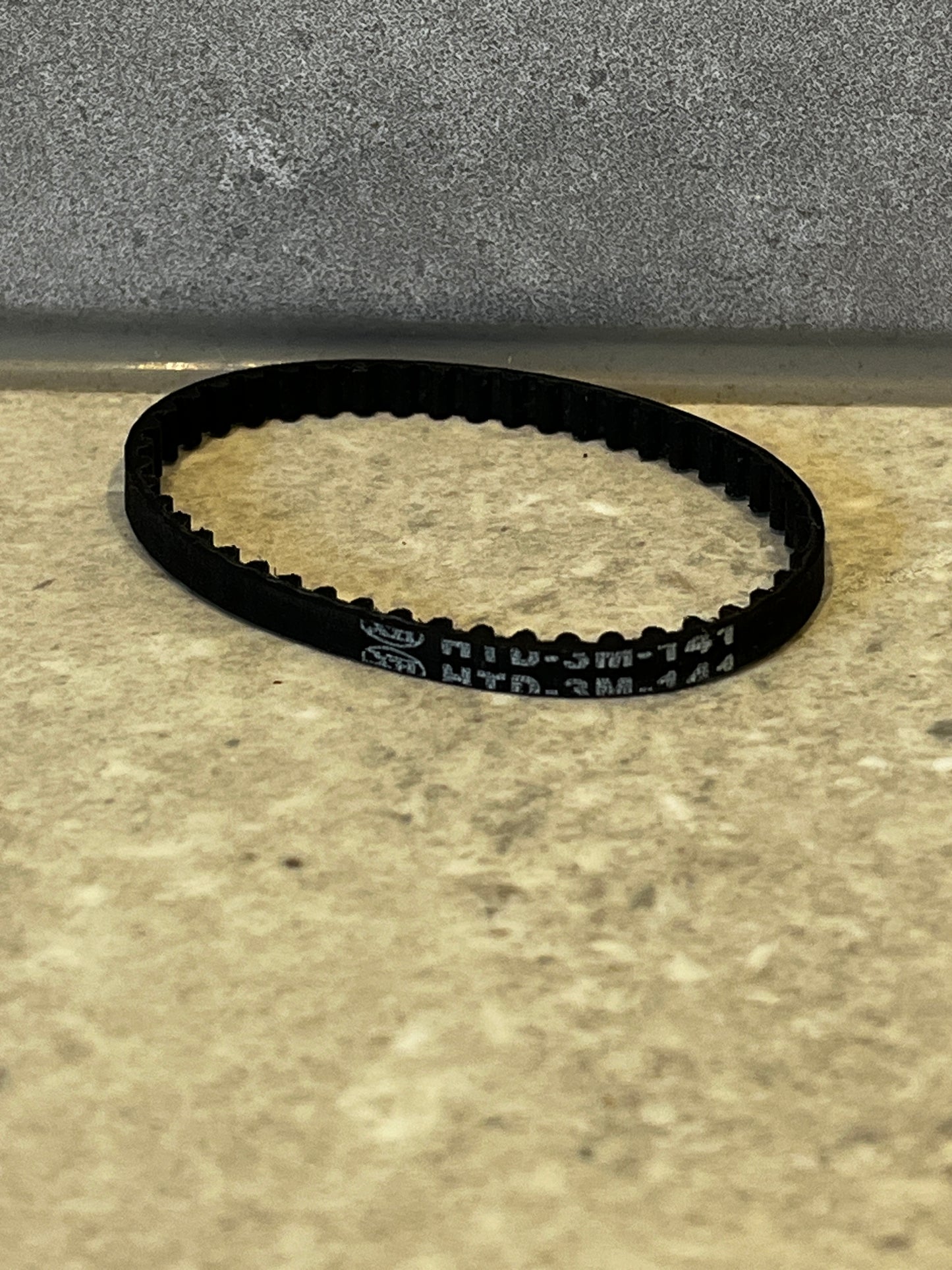 Close-up of black rubber timing belt with internal teeth on a beige surface