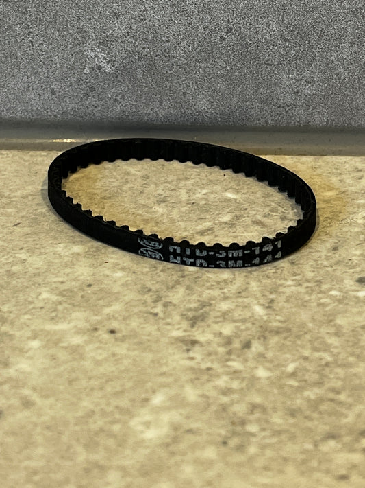 Close-up of black rubber timing belt with internal teeth on a beige surface