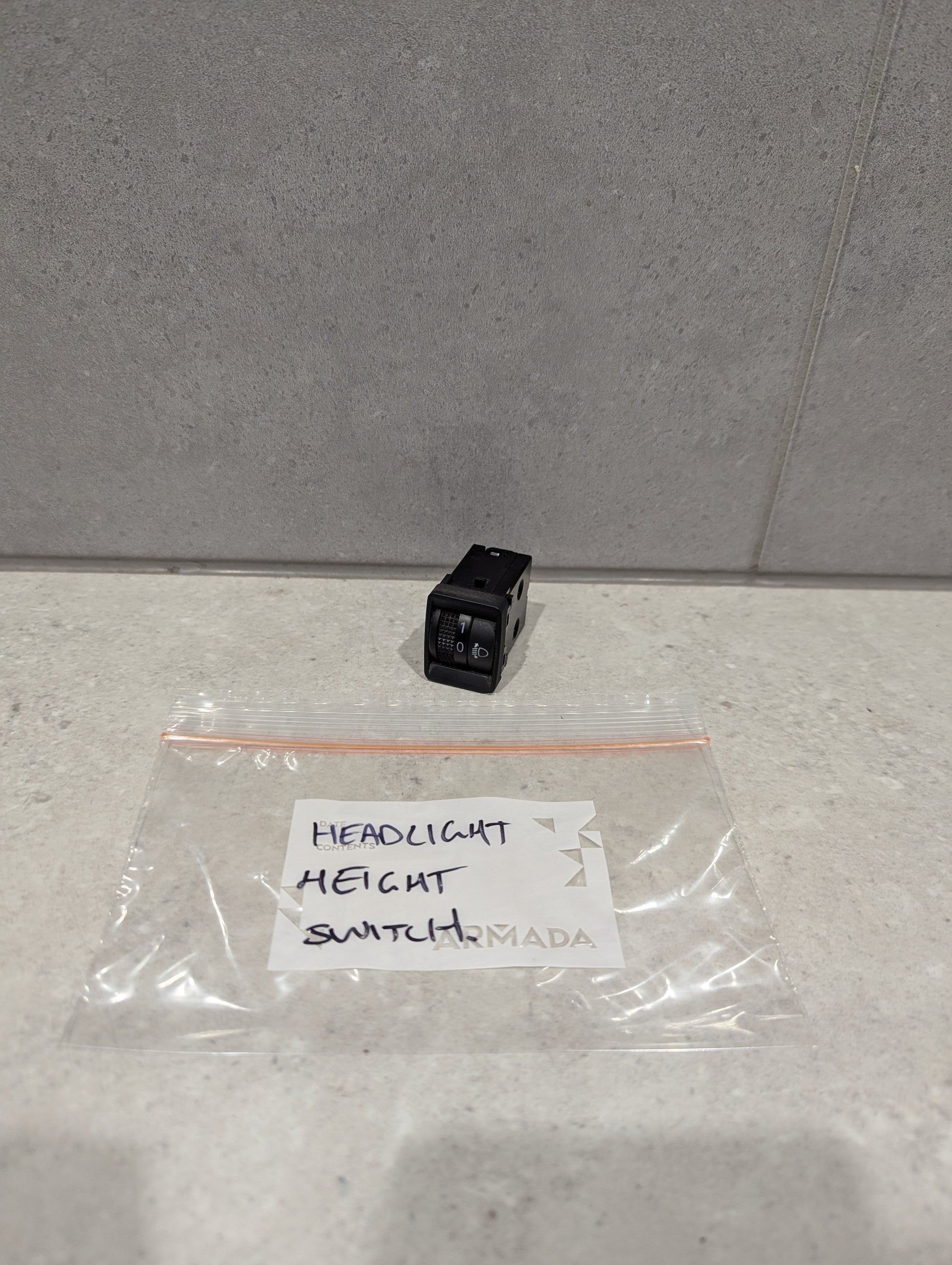 Black headlight height switch with labeled plastic bag on light countertop