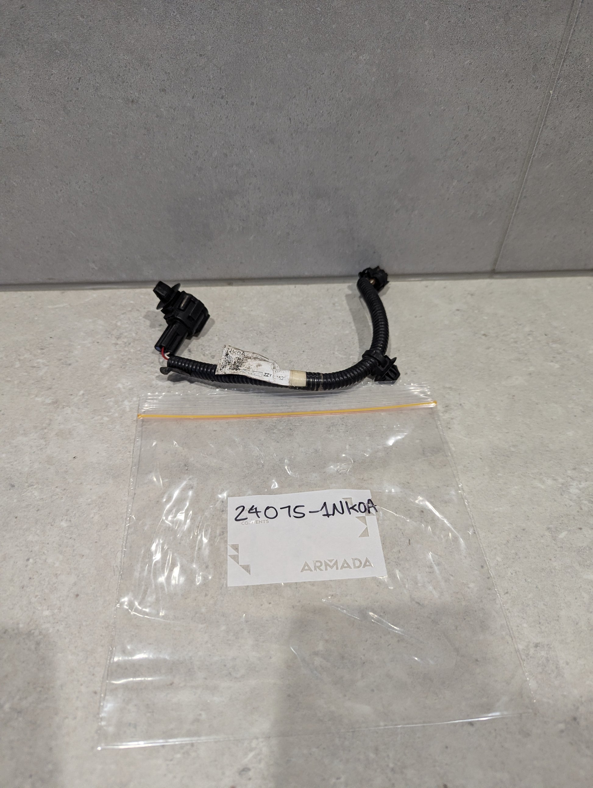 Automotive wiring harness connector assembly with black connectors and plastic bag labeled 24075-1NK0A