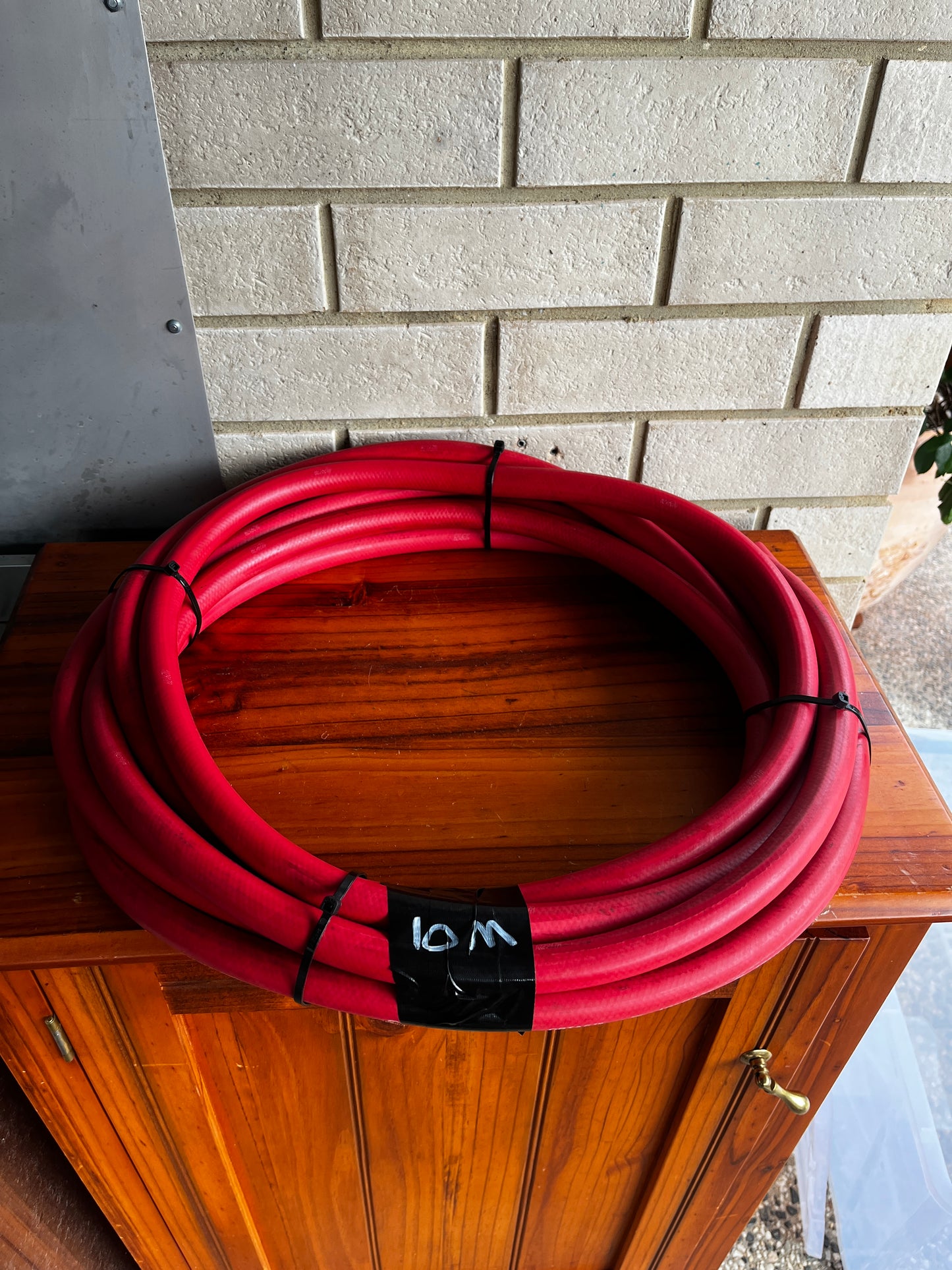 Coiled red Continental ContiTech ORTAC industrial hose on wooden cabinet