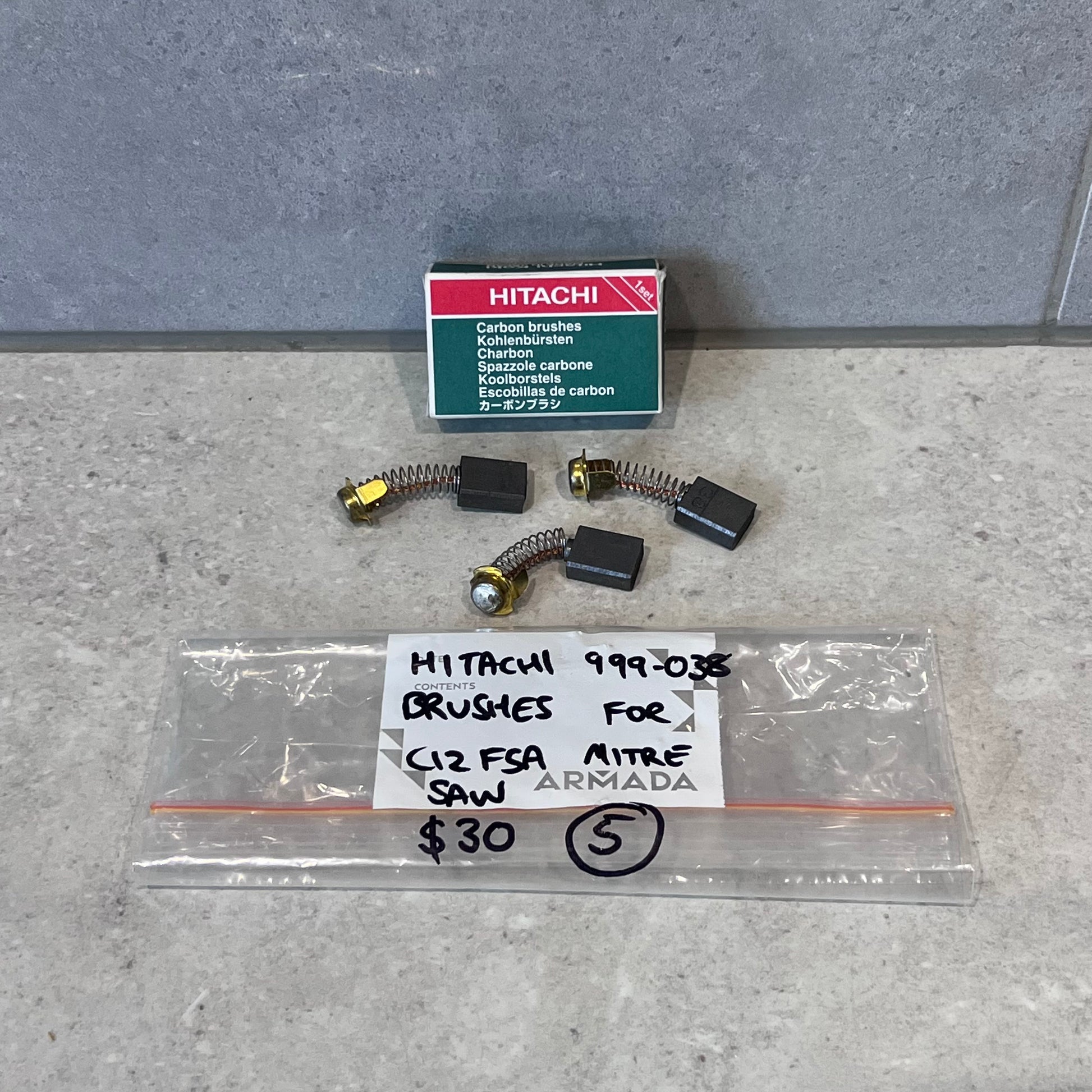 Hitachi 999-038 carbon brushes set with box for C12 FSA mitre saw, laid out on countertop