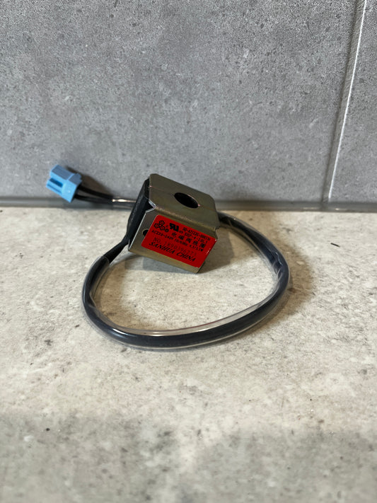 Industrial solenoid coil with metal housing and blue connector on gray tile background