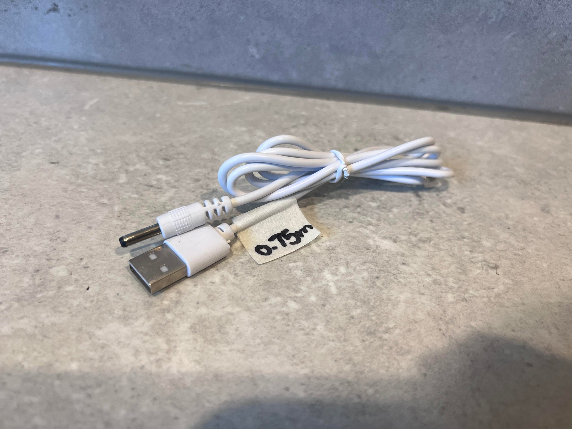 White USB to barrel charger cable coiled on a countertop