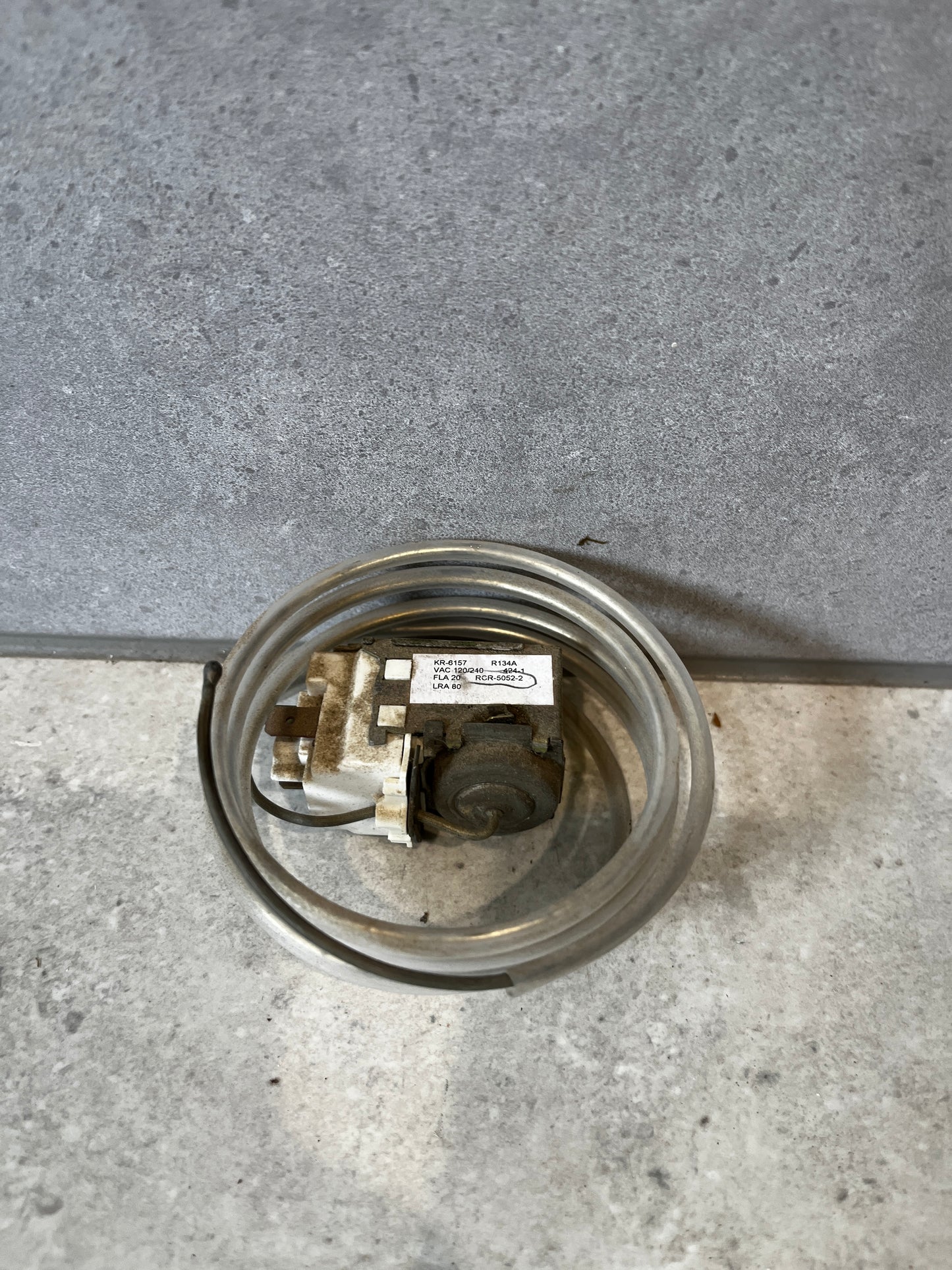 Refrigerator temperature control thermostat with coiled sensor on a gray surface
