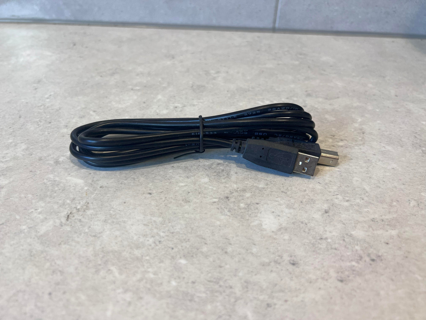 Coiled black USB A to USB B cable displayed on a light surface