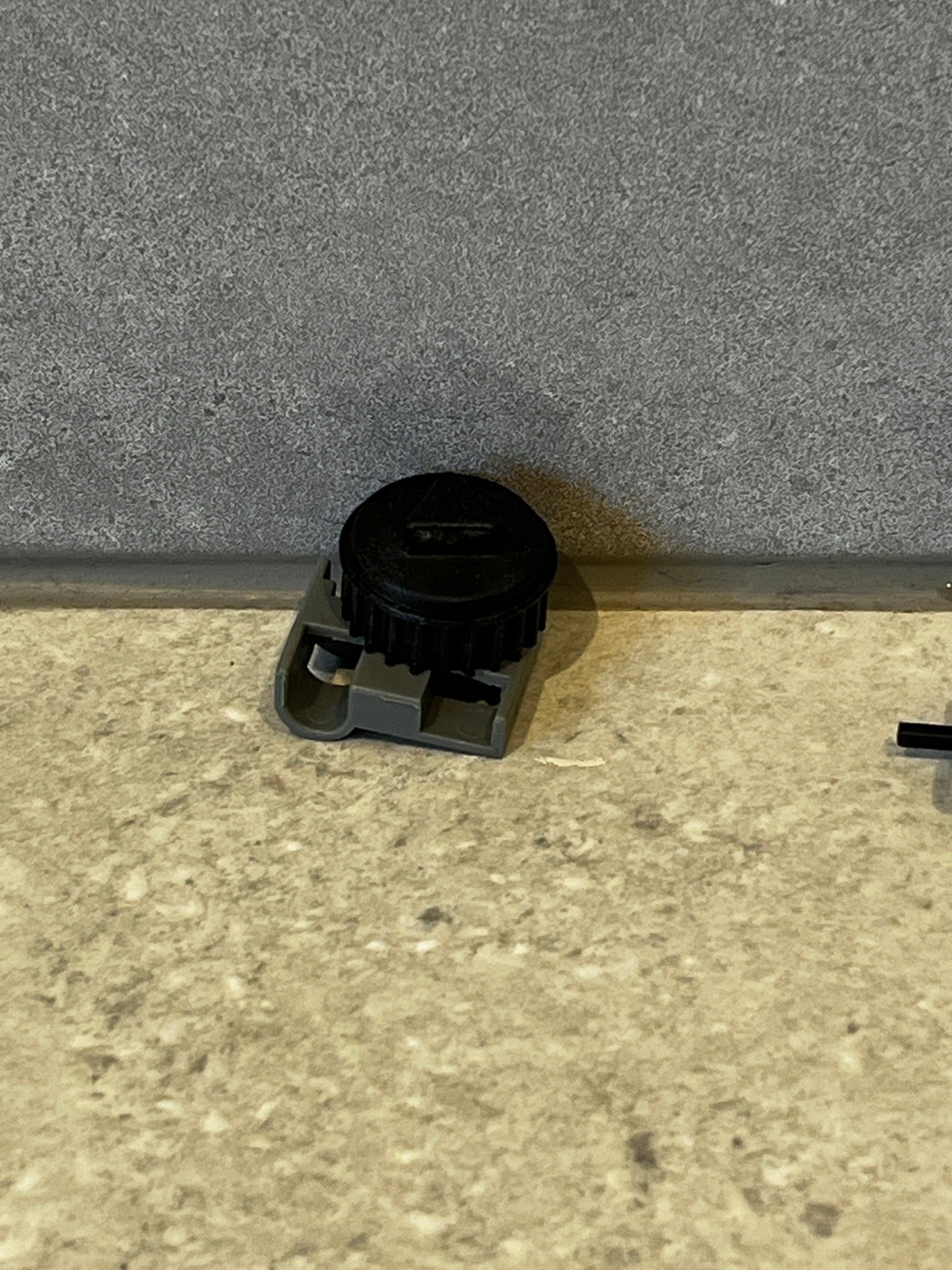 Adjustable plastic gear component with black rotating wheel and gray base resting on a textured surface