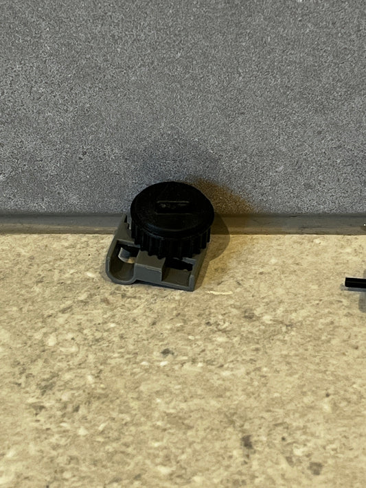 Adjustable plastic gear component with black rotating wheel and gray base resting on a textured surface
