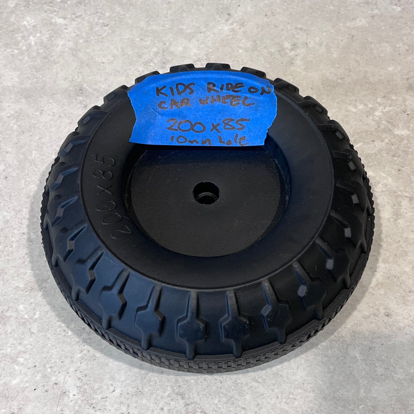 Black plastic replacement wheel for kids ride-on car, 200x85 mm size, with center hole and treaded pattern