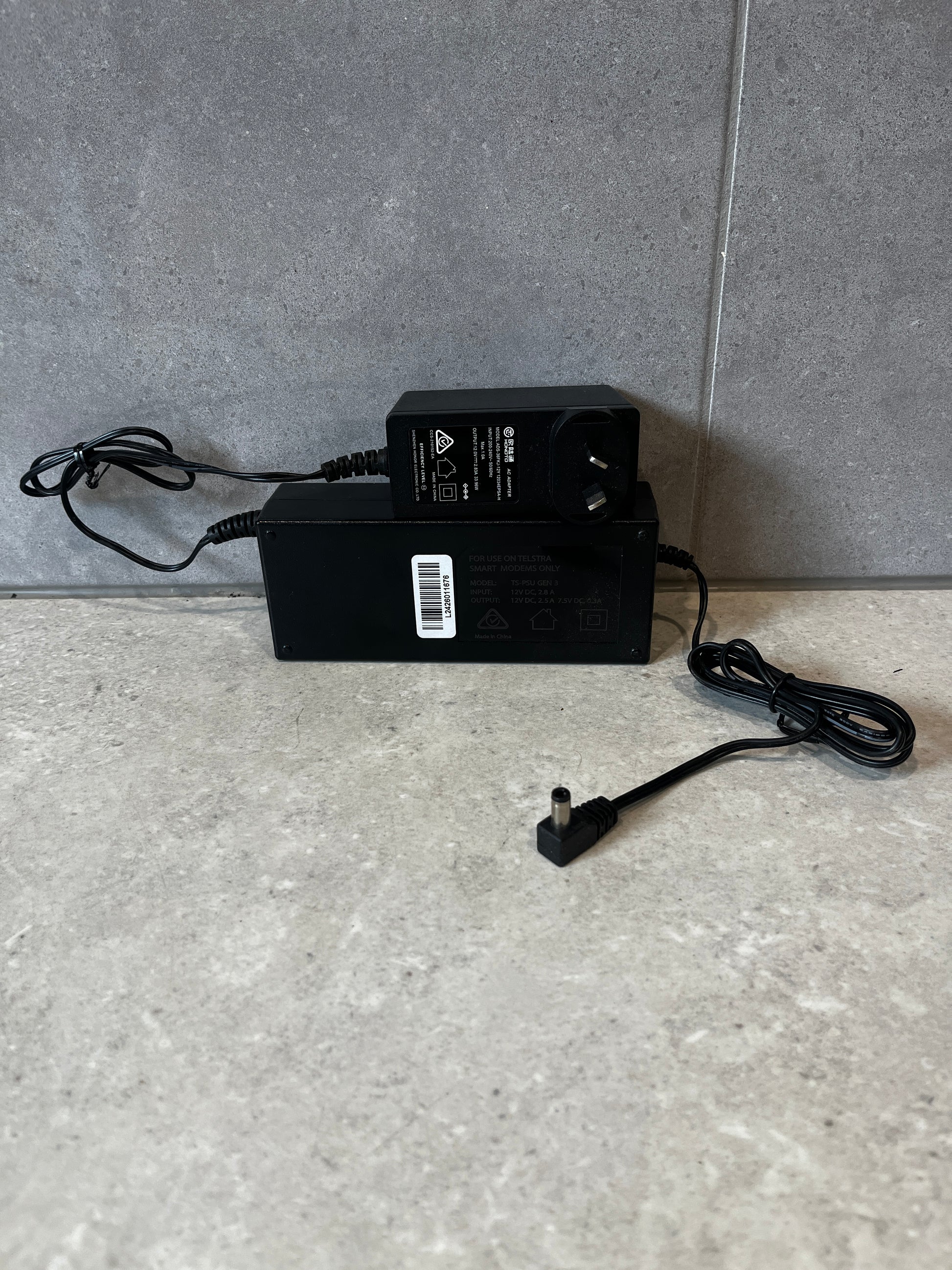 Two black Telstra smart modem power adapters on a stone surface