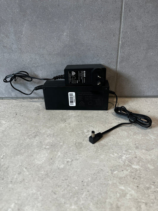 Two black Telstra smart modem power adapters on a stone surface