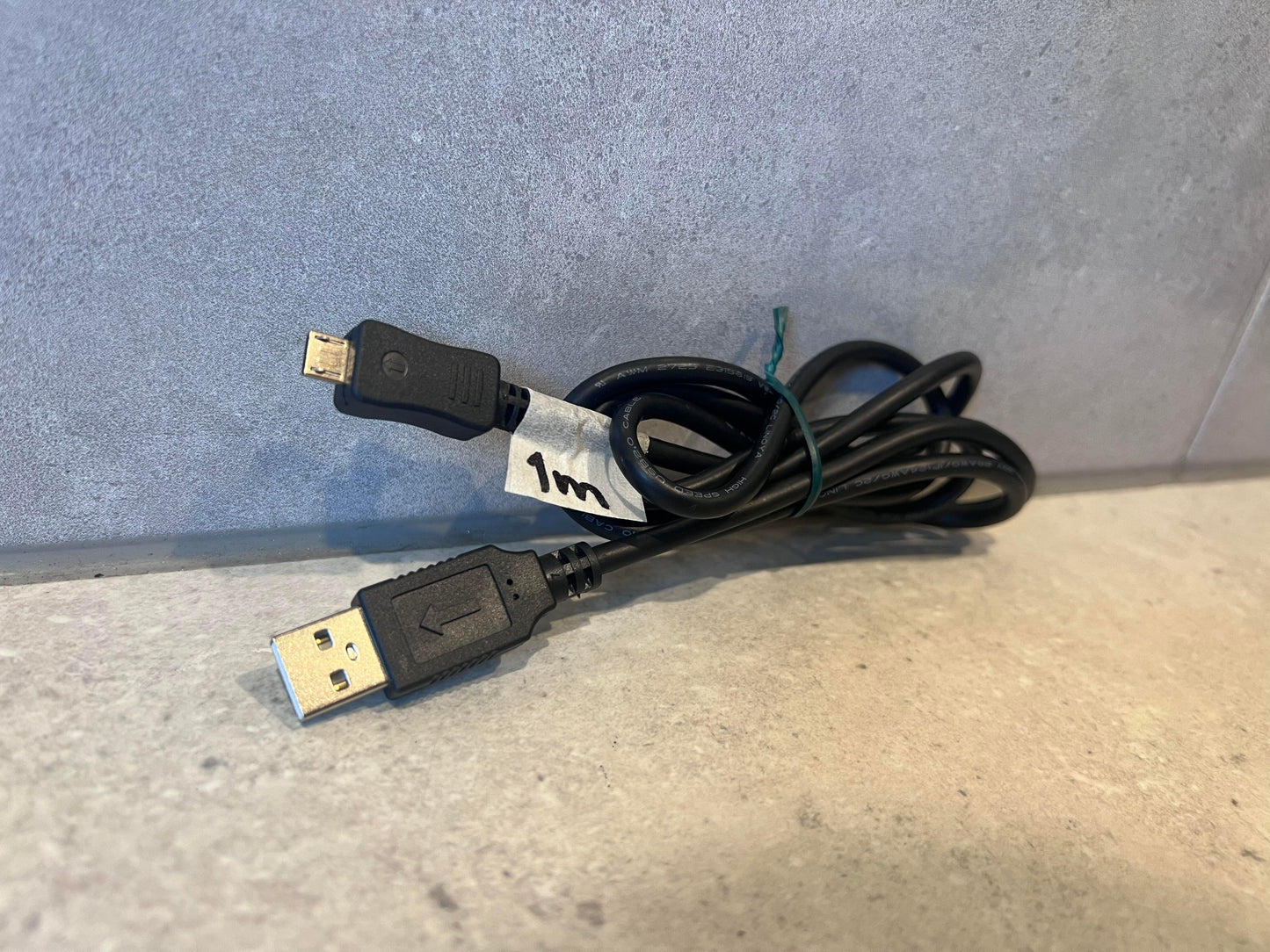 Coiled black USB to Micro USB charging cable with 1m label on stone background