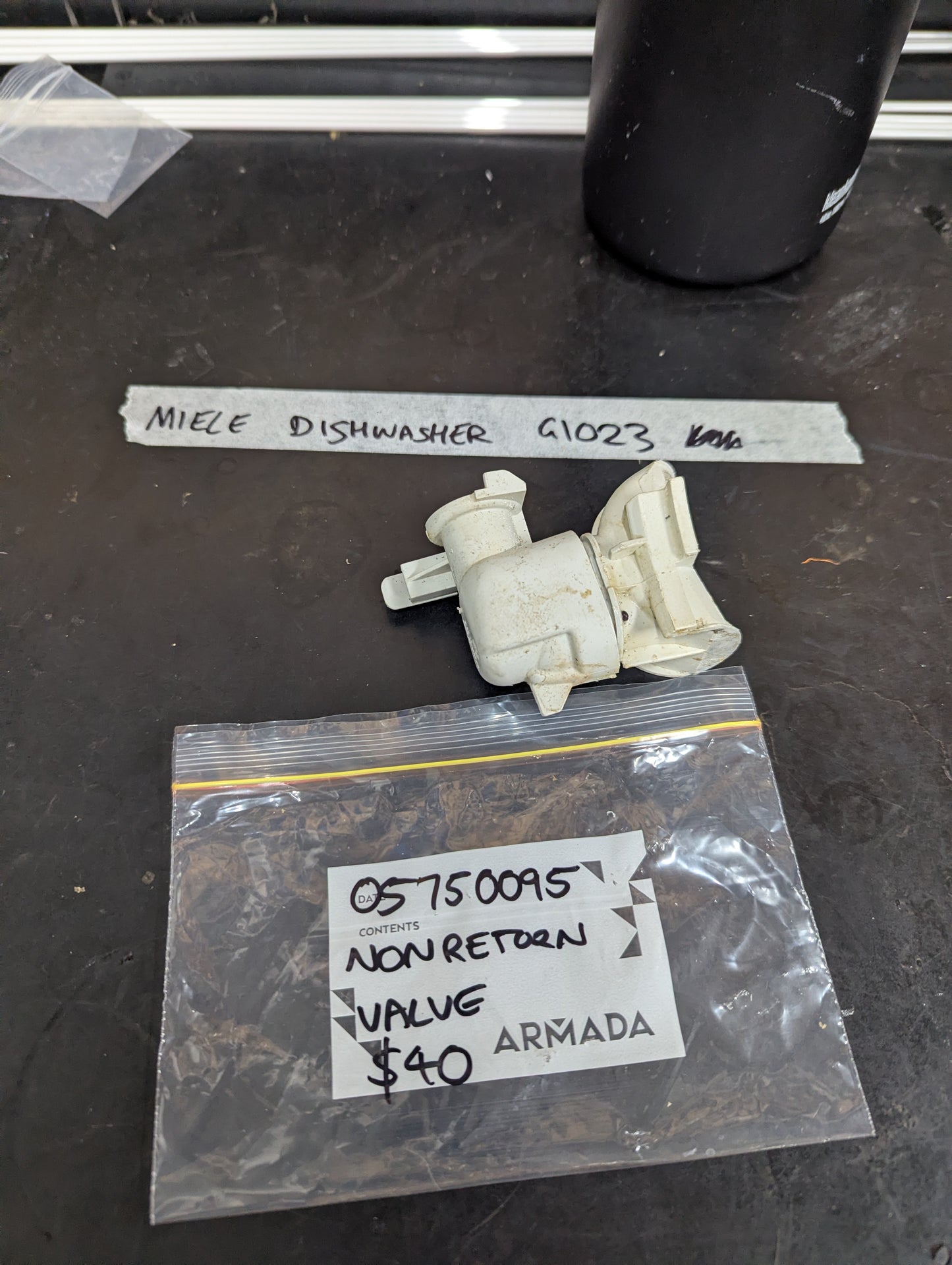 Miele Dishwasher G1023 non return valve with labeled bag and valve on black surface