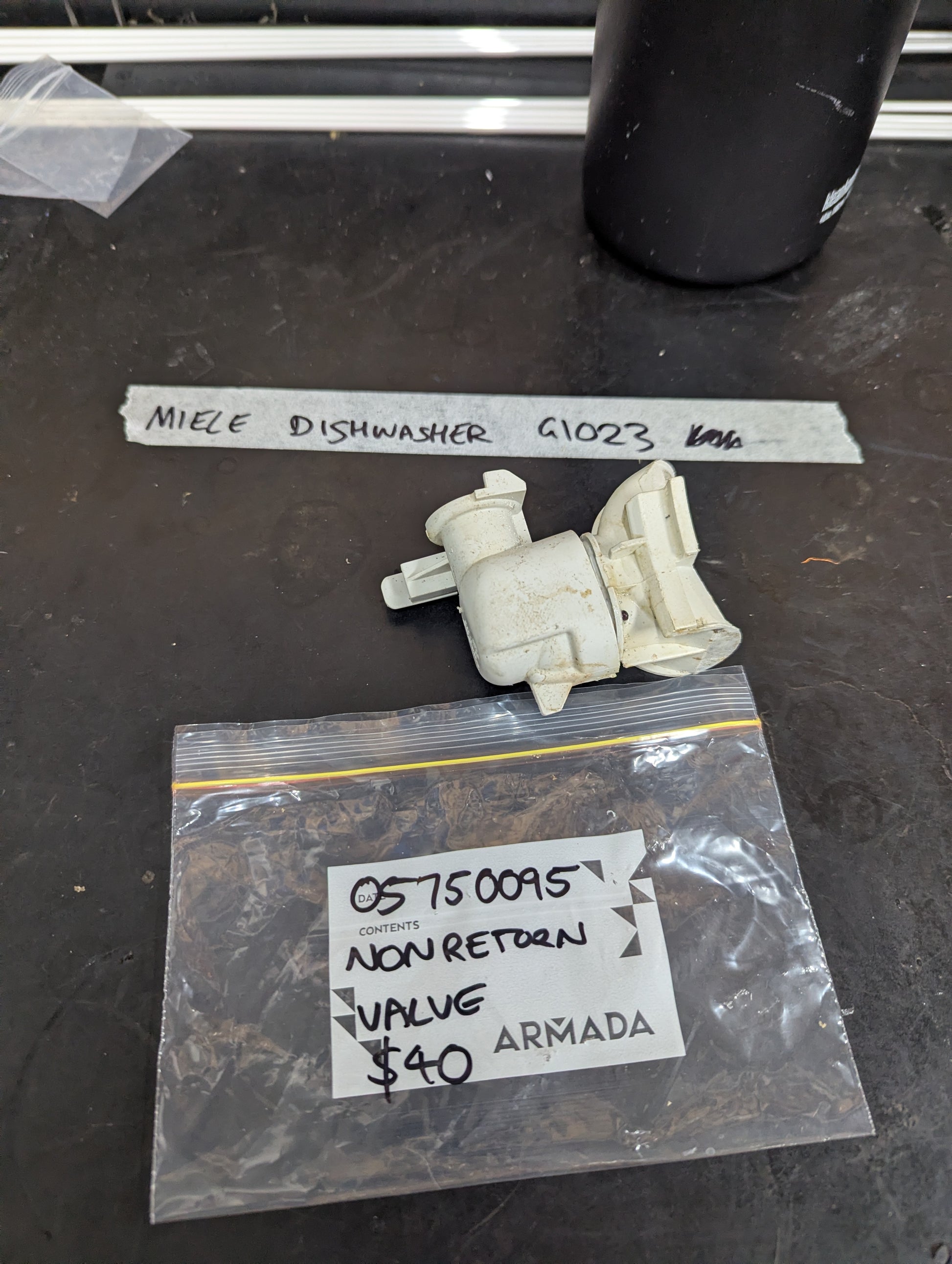 Miele Dishwasher G1023 non return valve with labeled bag and valve on black surface
