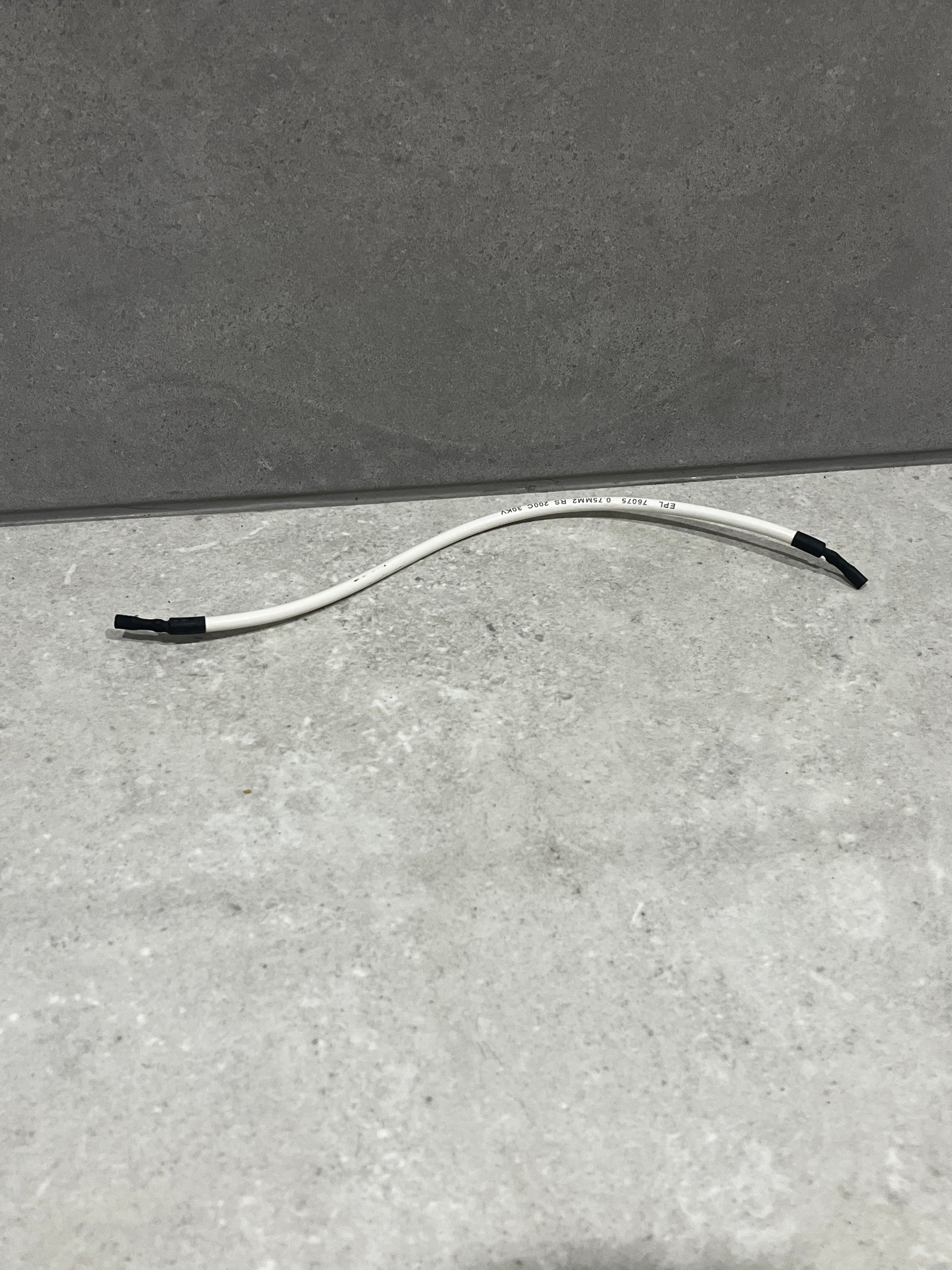 White insulated electrical wire with black-taped ends lying on a gray surface