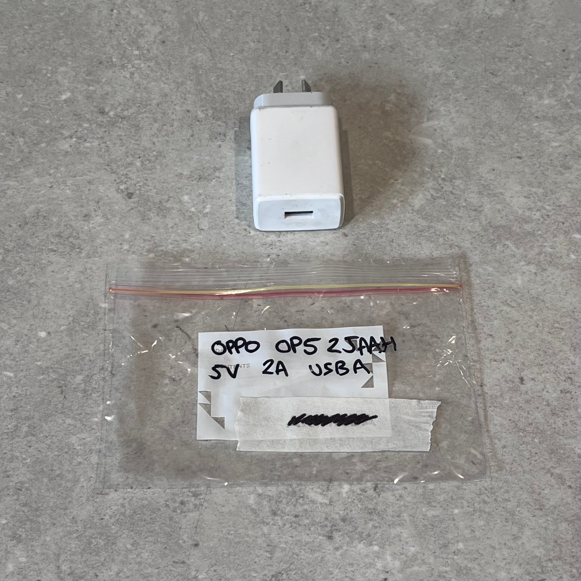 Oppo 5V 2A USB-A wall charger and labeled plastic bag on gray surface