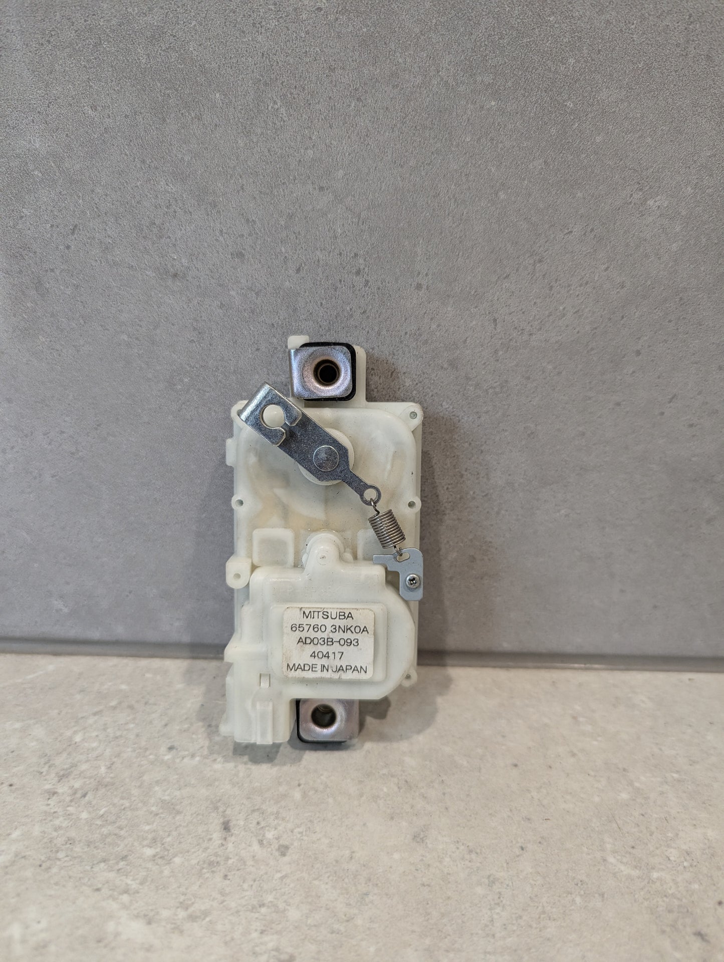 Front view of Mitsuba door lock actuator assembly with spring and label