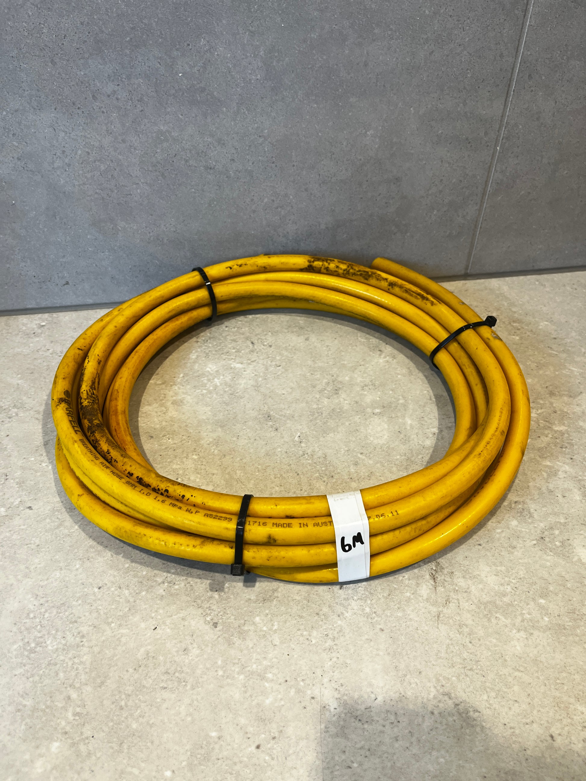 Coiled yellow Barfell breathing air hose secured with black zip ties on floor