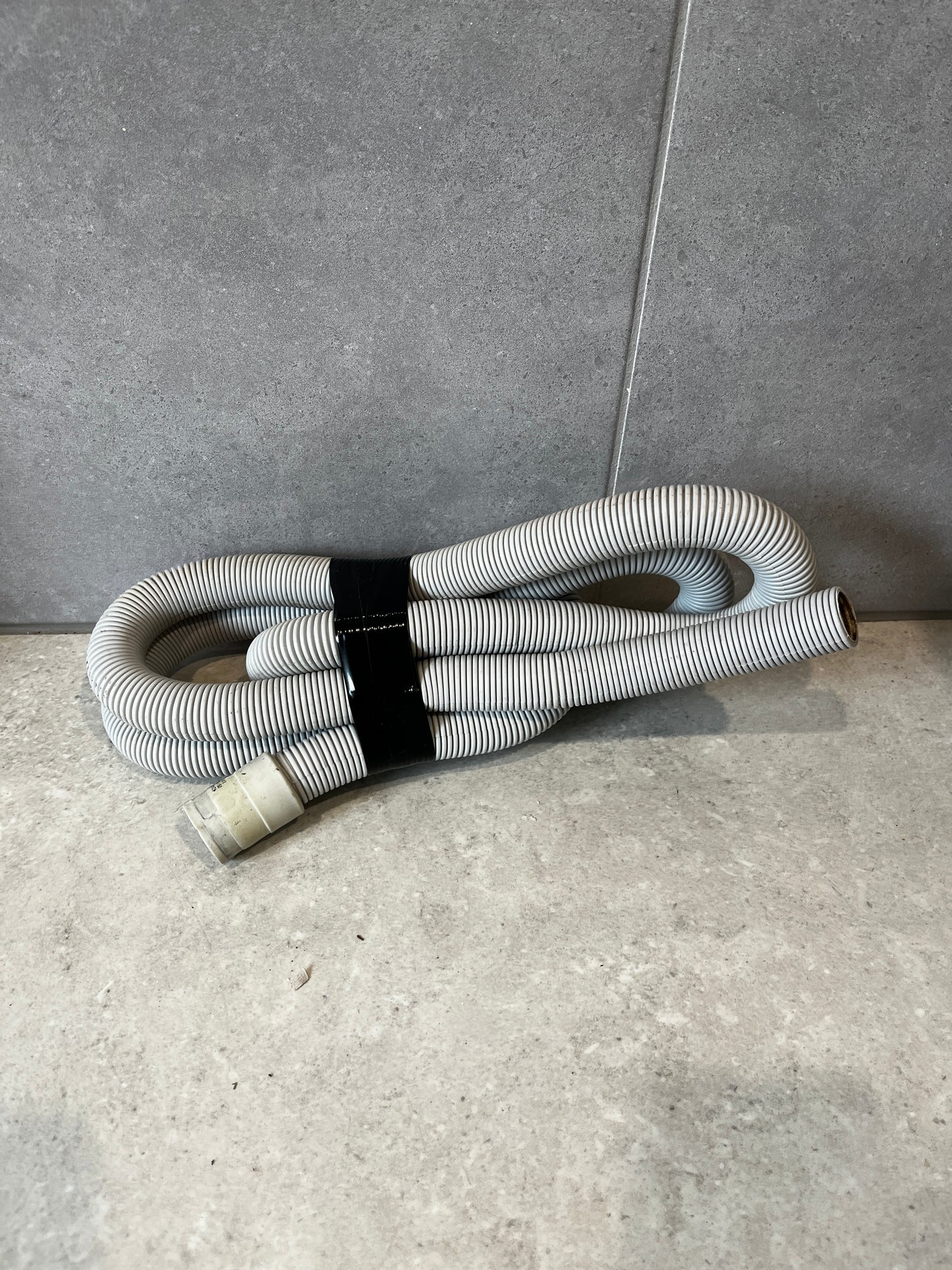 Flexible corrugated plastic drain hose coiled on a tiled floor