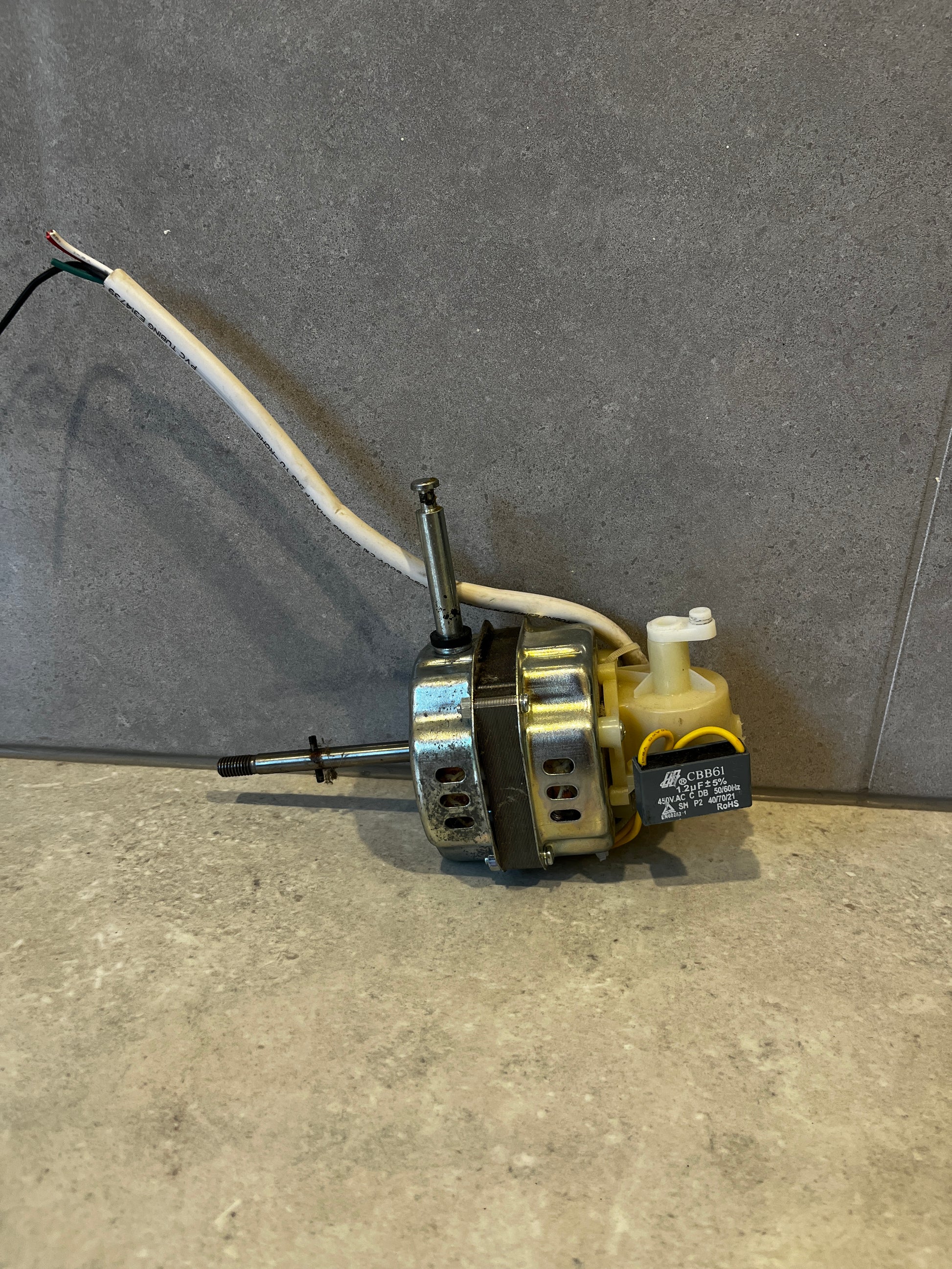 Electric motor with capacitor and attached white wires laying on grey surface