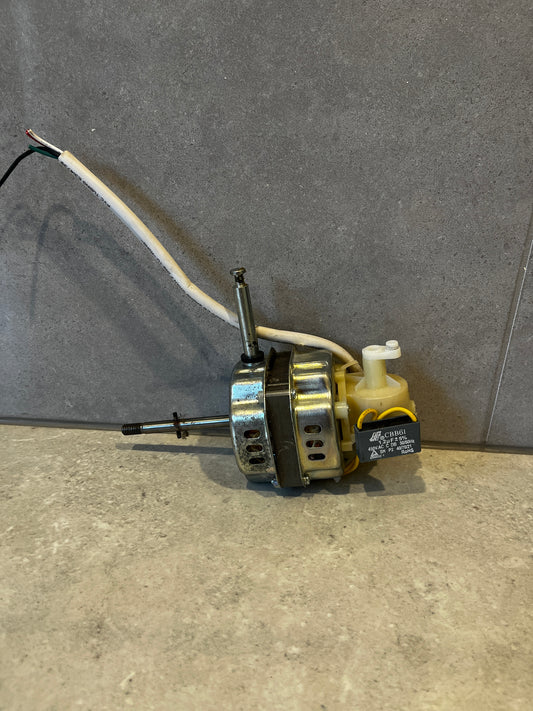 Electric motor with capacitor and attached white wires laying on grey surface