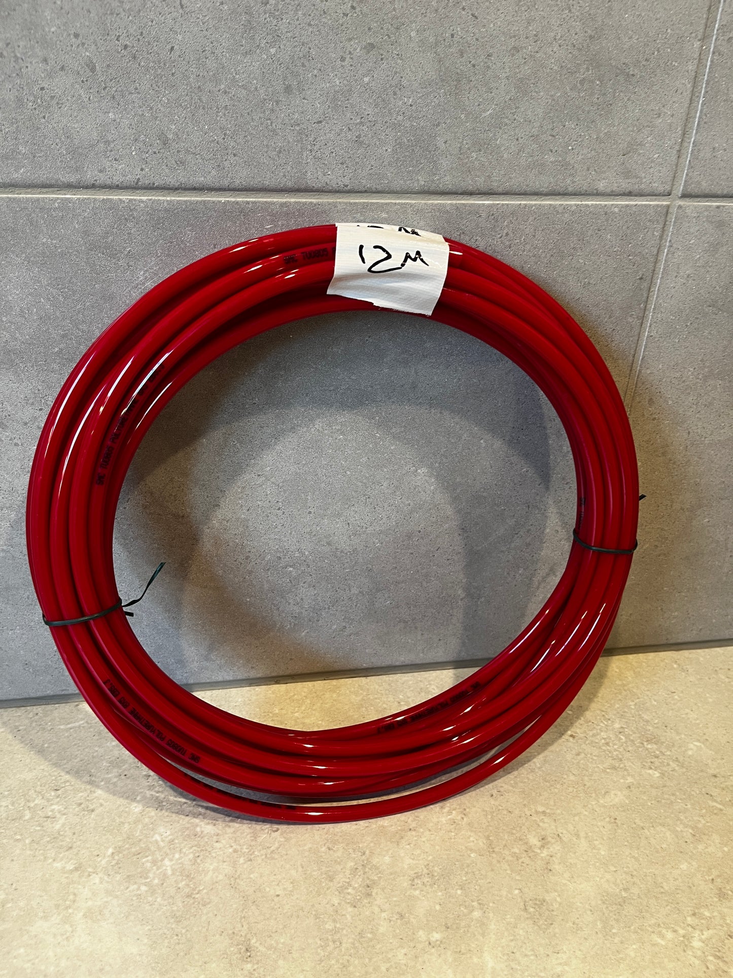 Coiled 12 meter red polyurethane tubing laid on floor with tape marked '12M'