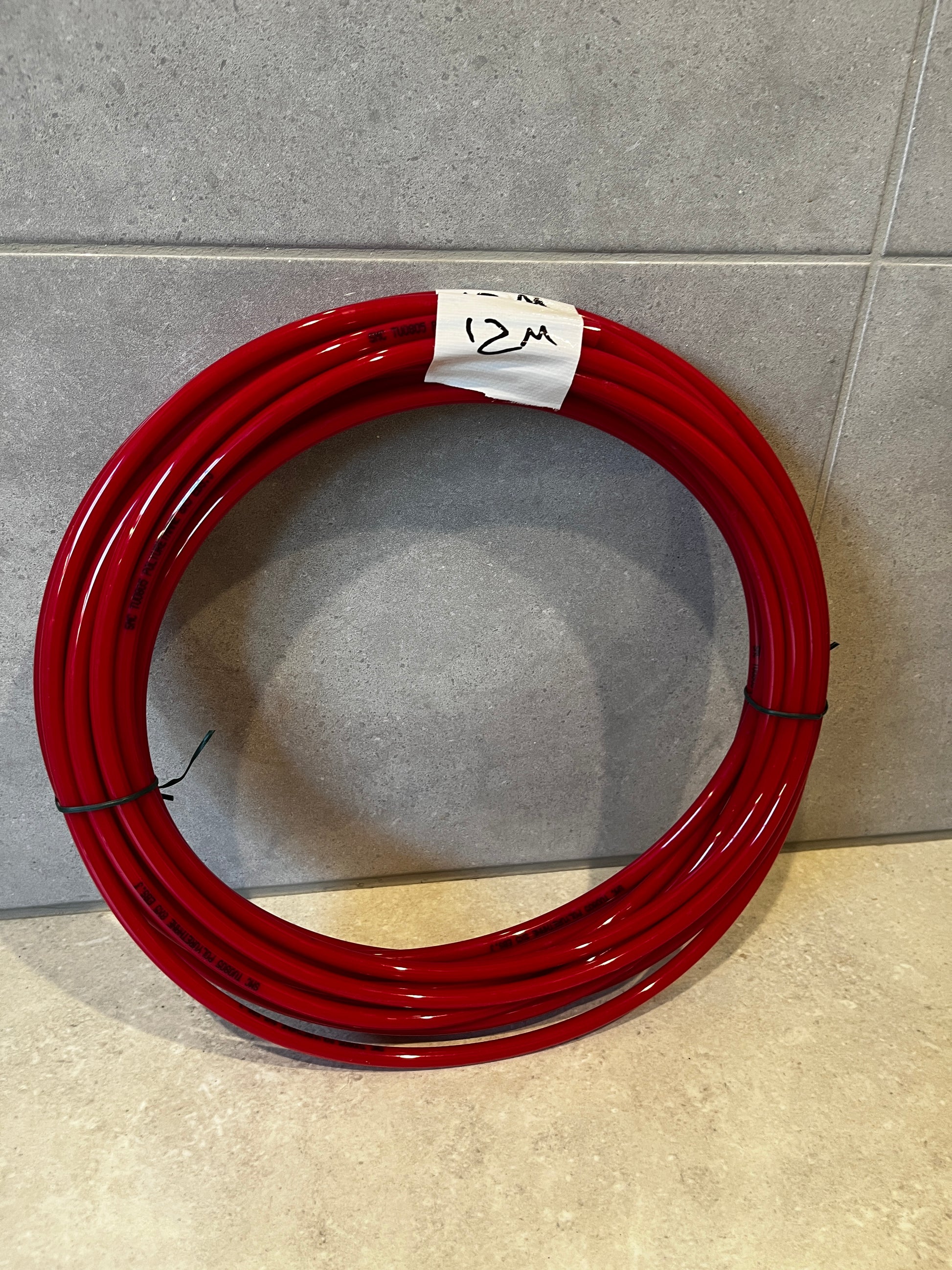 Coiled 12 meter red polyurethane tubing laid on floor with tape marked '12M'