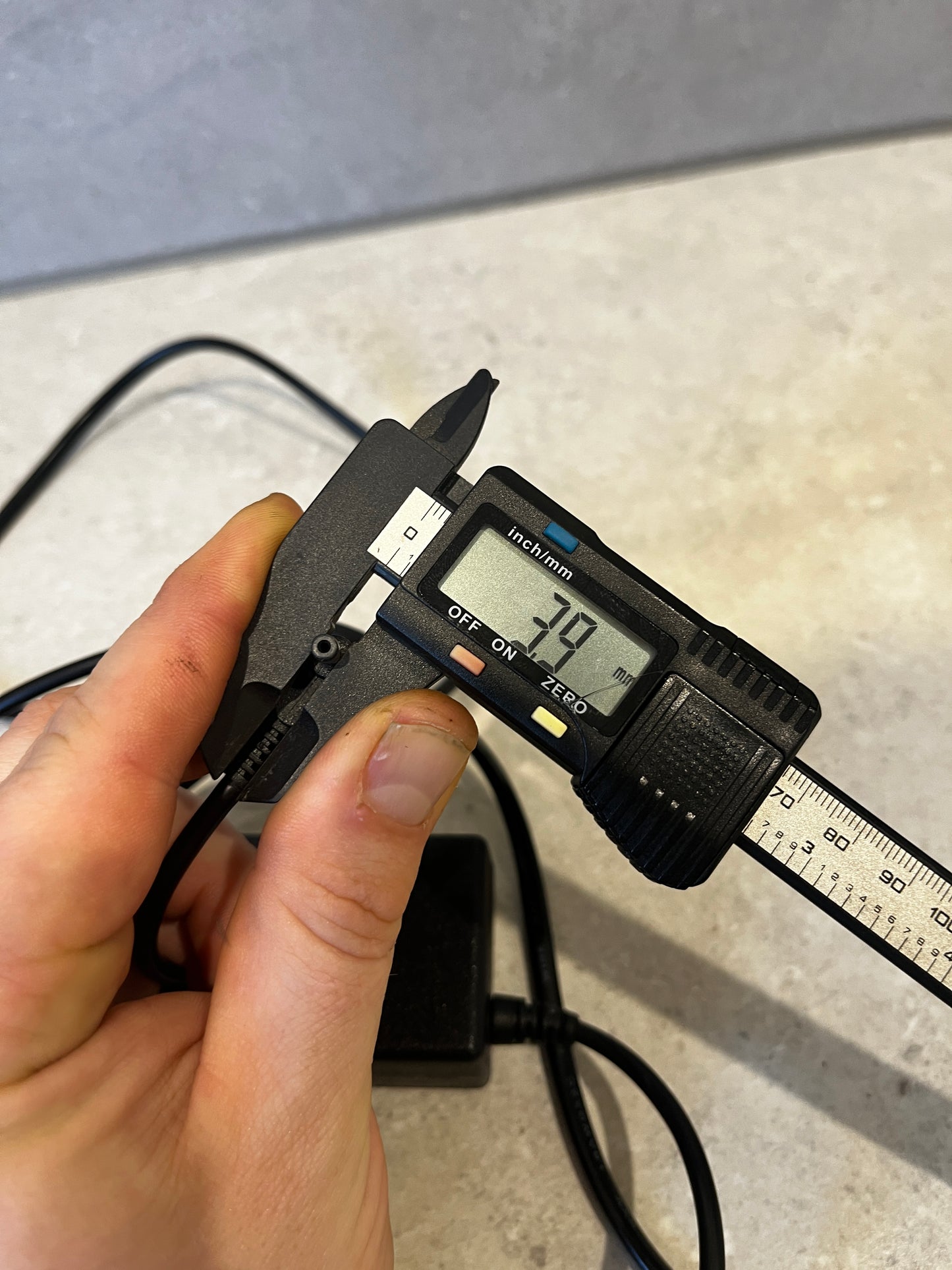 Hand holding digital caliper measuring AC adapter connector diameter at 7.9mm