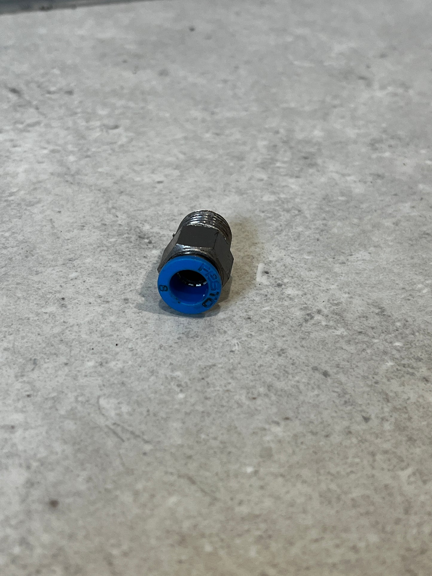 Metal push-to-connect pneumatic fitting with blue ring on gray surface front view