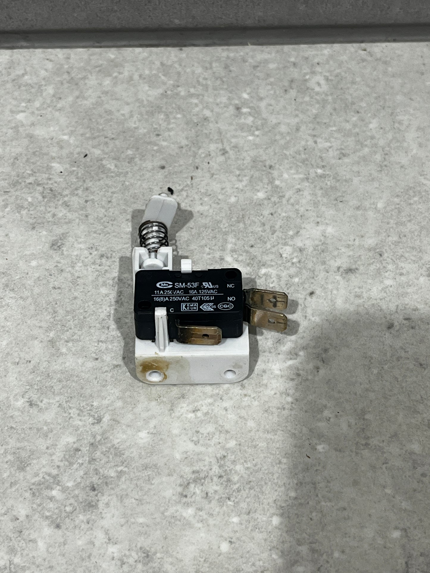 Close-up of SM-53F micro switch with spring actuator mounted on white base showing metal terminals