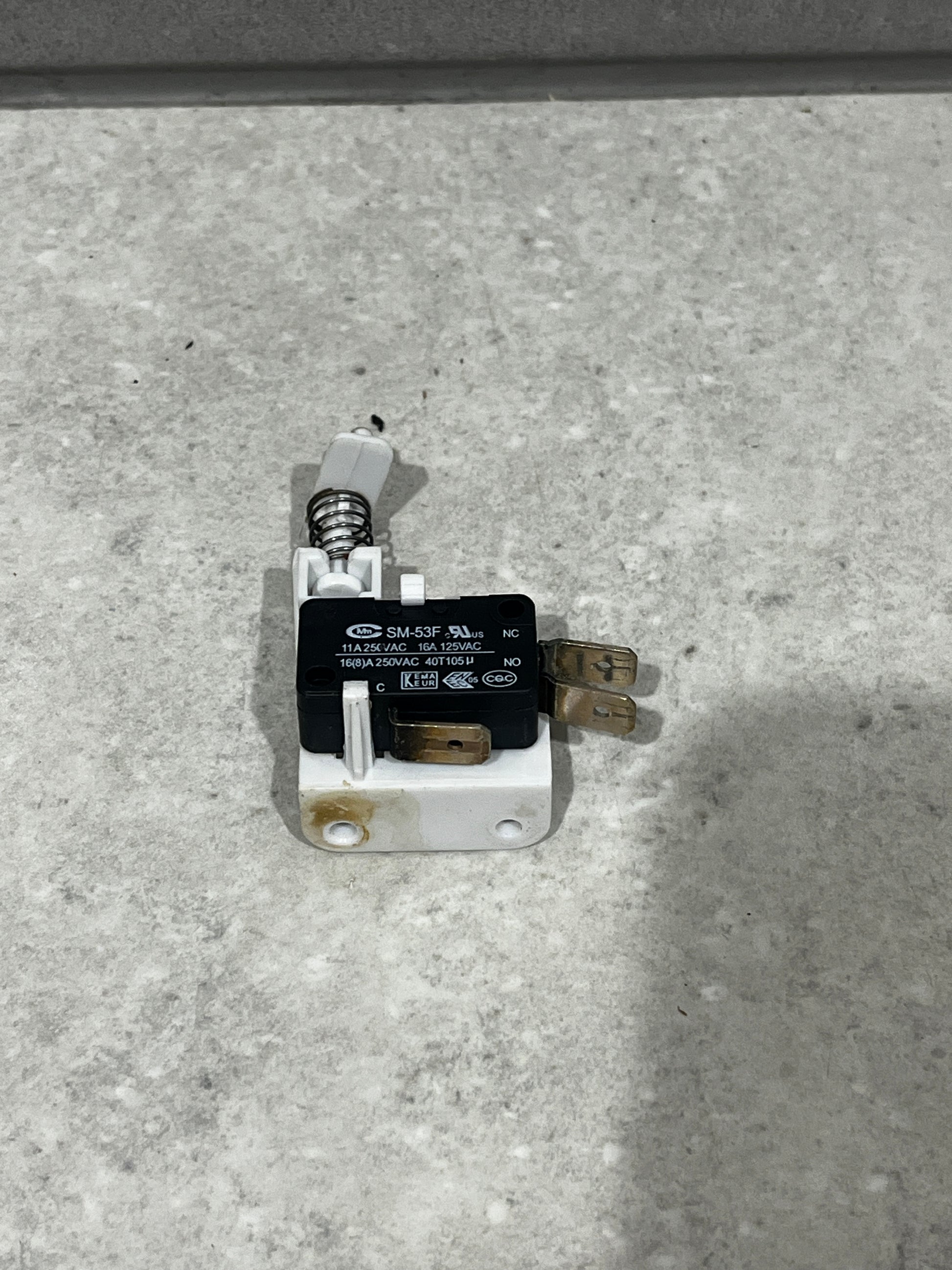 Close-up of SM-53F micro switch with spring actuator mounted on white base showing metal terminals