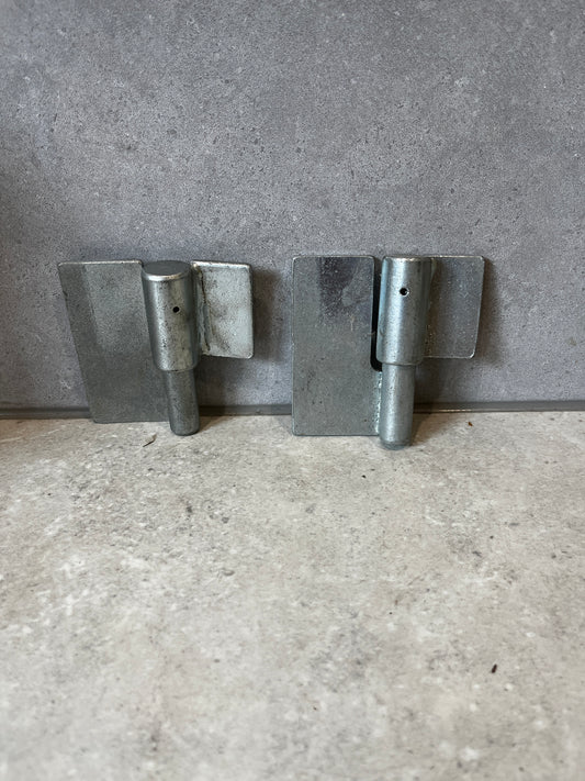 Set of two heavy-duty metal gate hinges with galvanized finish on a stone surface