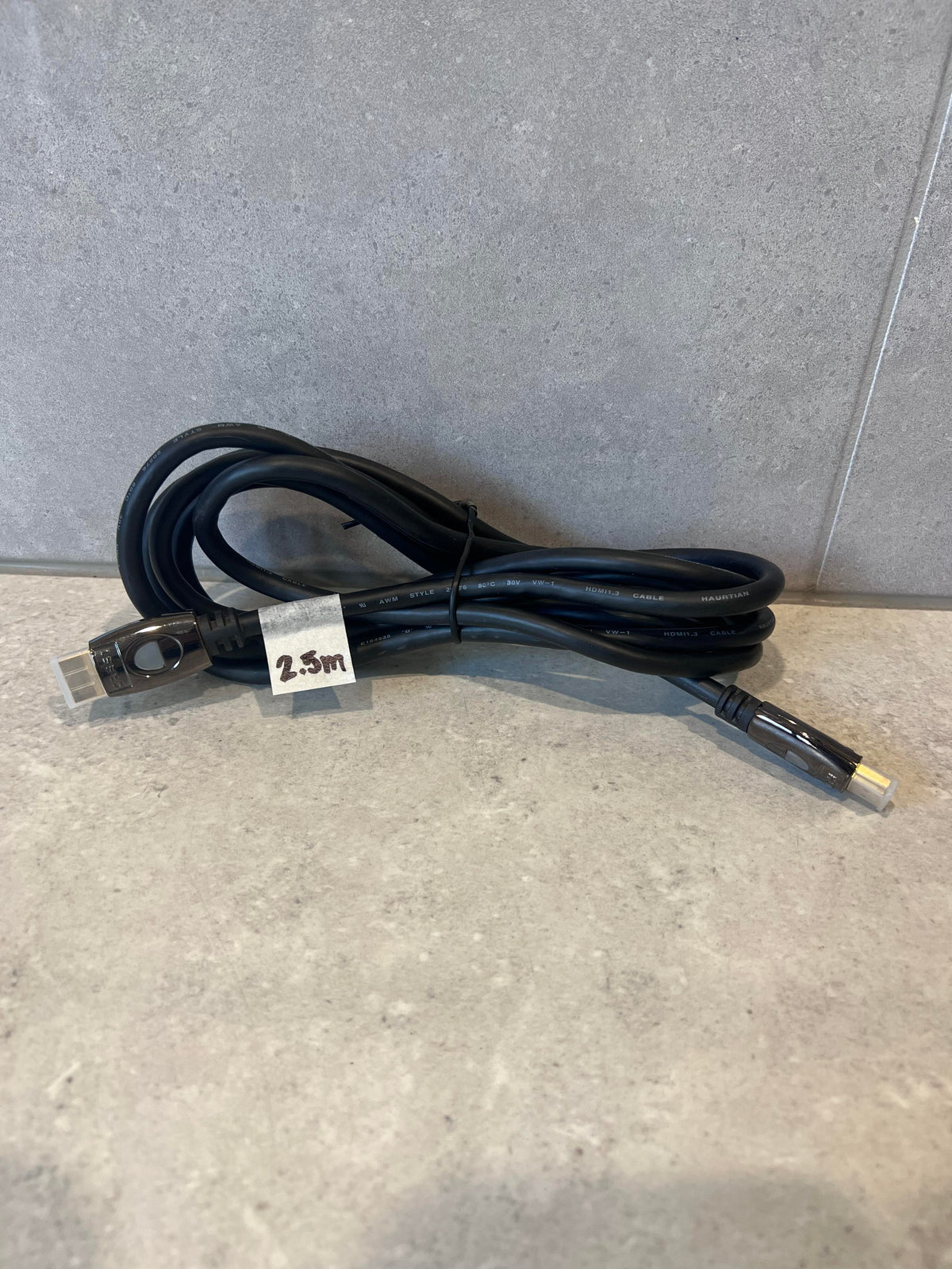 Coiled 2.5 meter HDMI cable with black connectors on stone surface