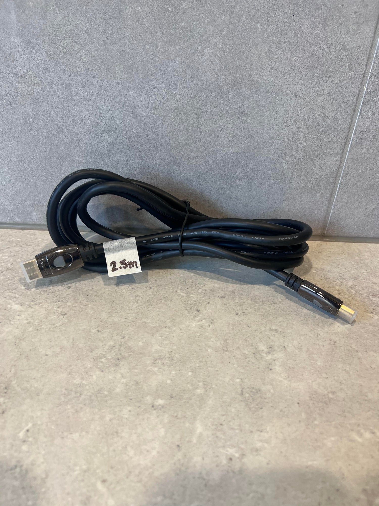 Coiled 2.5 meter HDMI cable with black connectors on stone surface