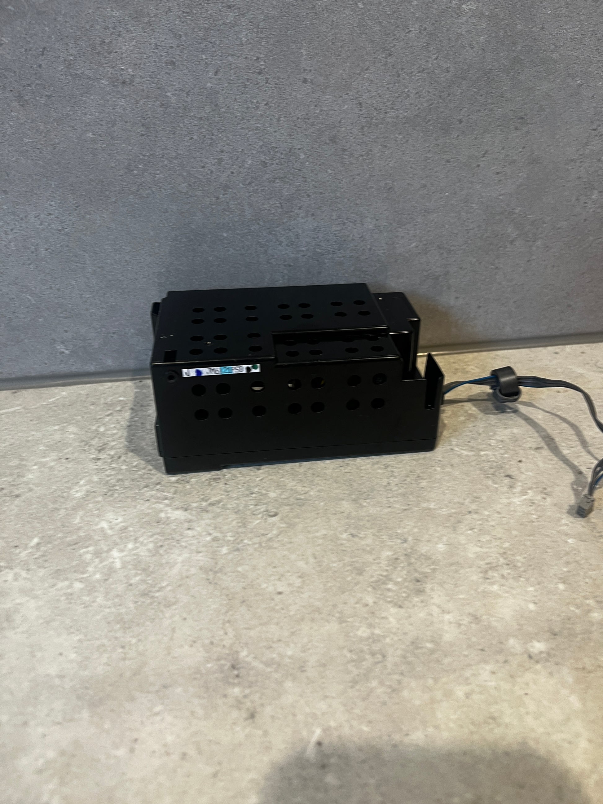 Black rectangular metal power supply unit with ventilation holes and attached cable on surface