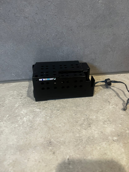 Black rectangular metal power supply unit with ventilation holes and attached cable on surface