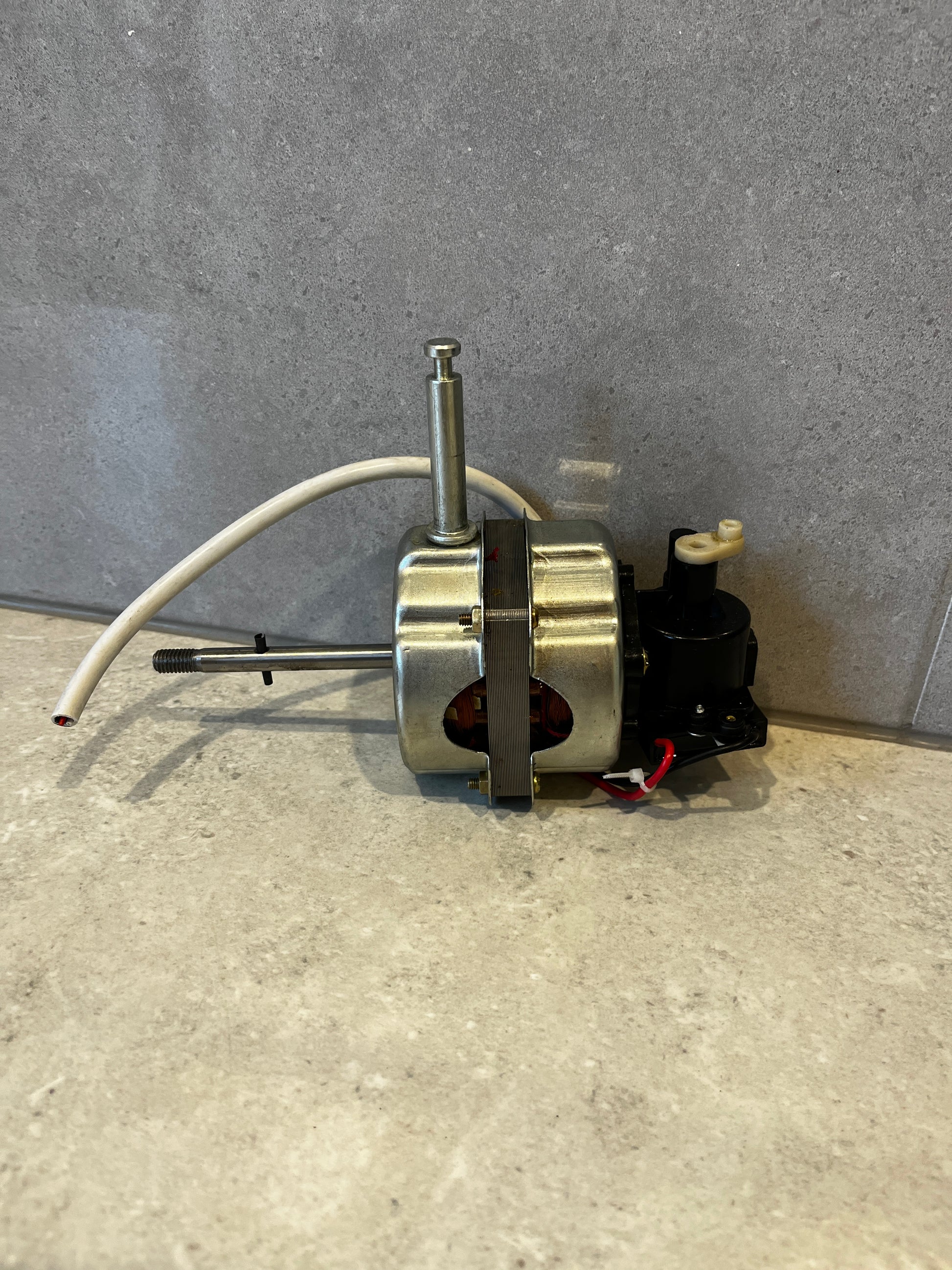 Side view of electric fan motor with metal housing and white wire against gray background