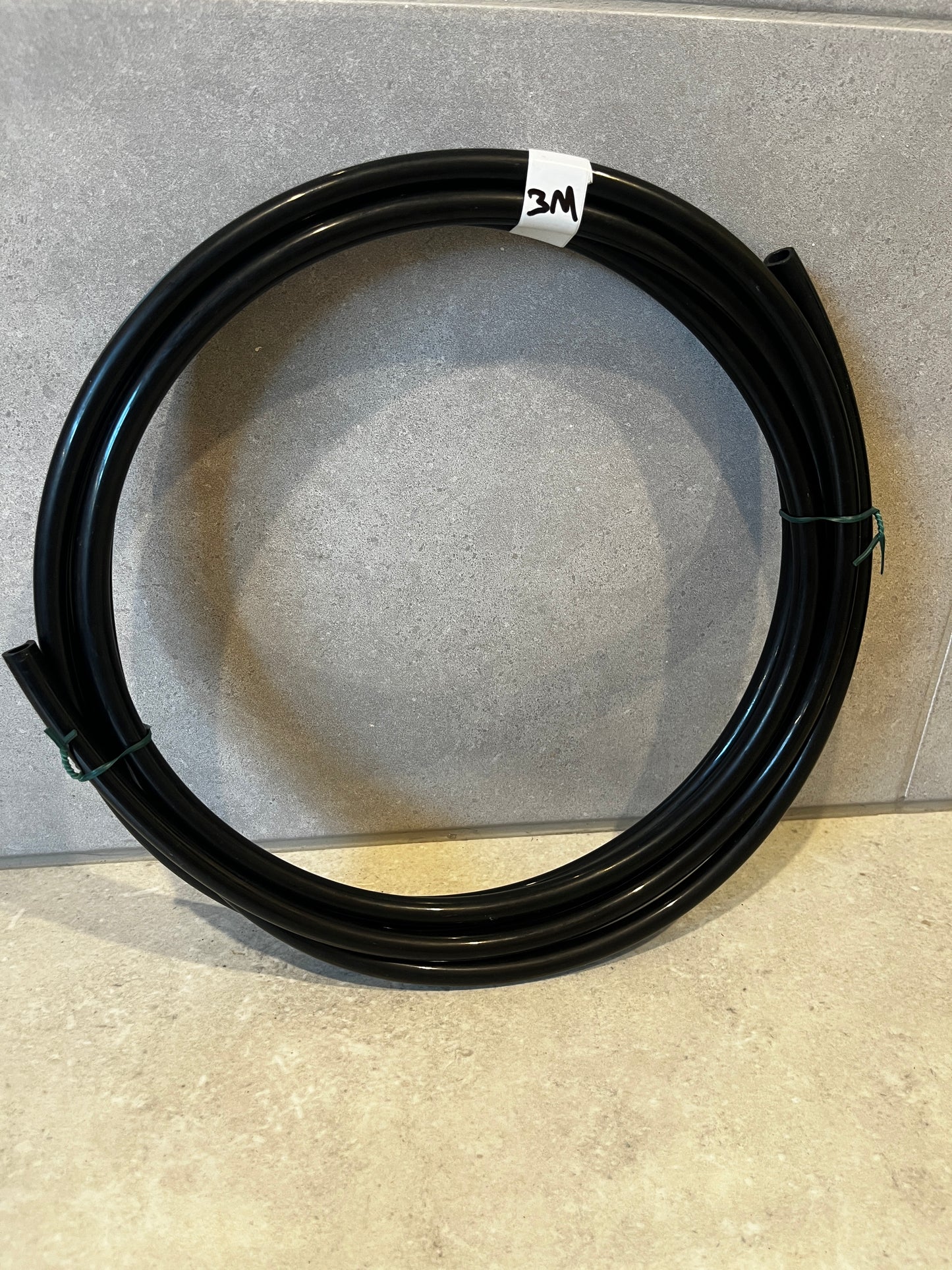 Coiled black flexible tubing 3 meter length on gray surface