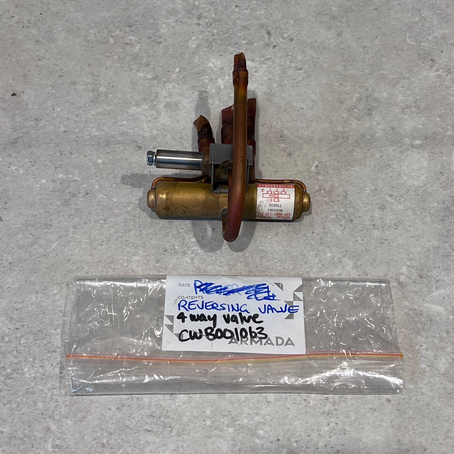 HVAC 4-way reversing valve with labeled storage bag on a light surface