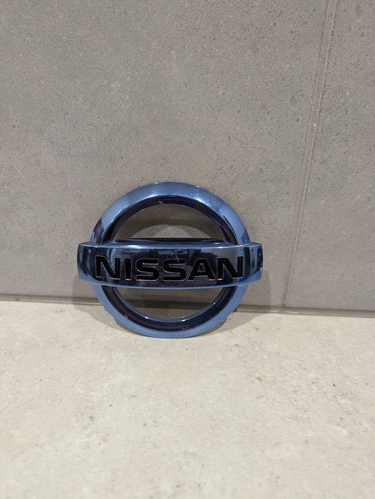 Nissan chrome vehicle emblem badge on light tile background