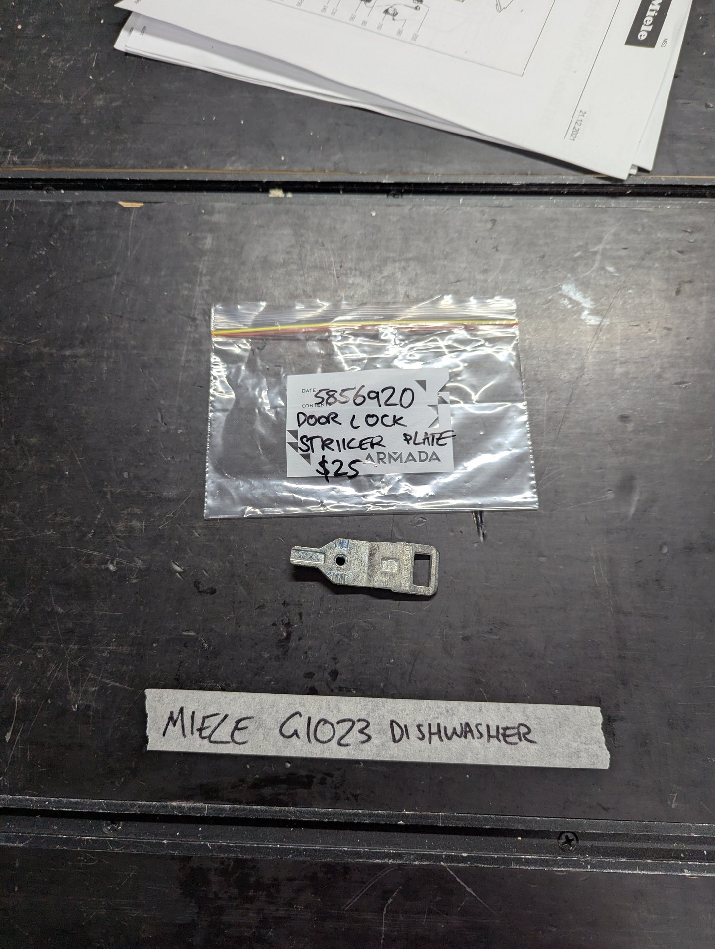 Miele G1023 dishwasher door lock striker plate with labeled packaging on a table